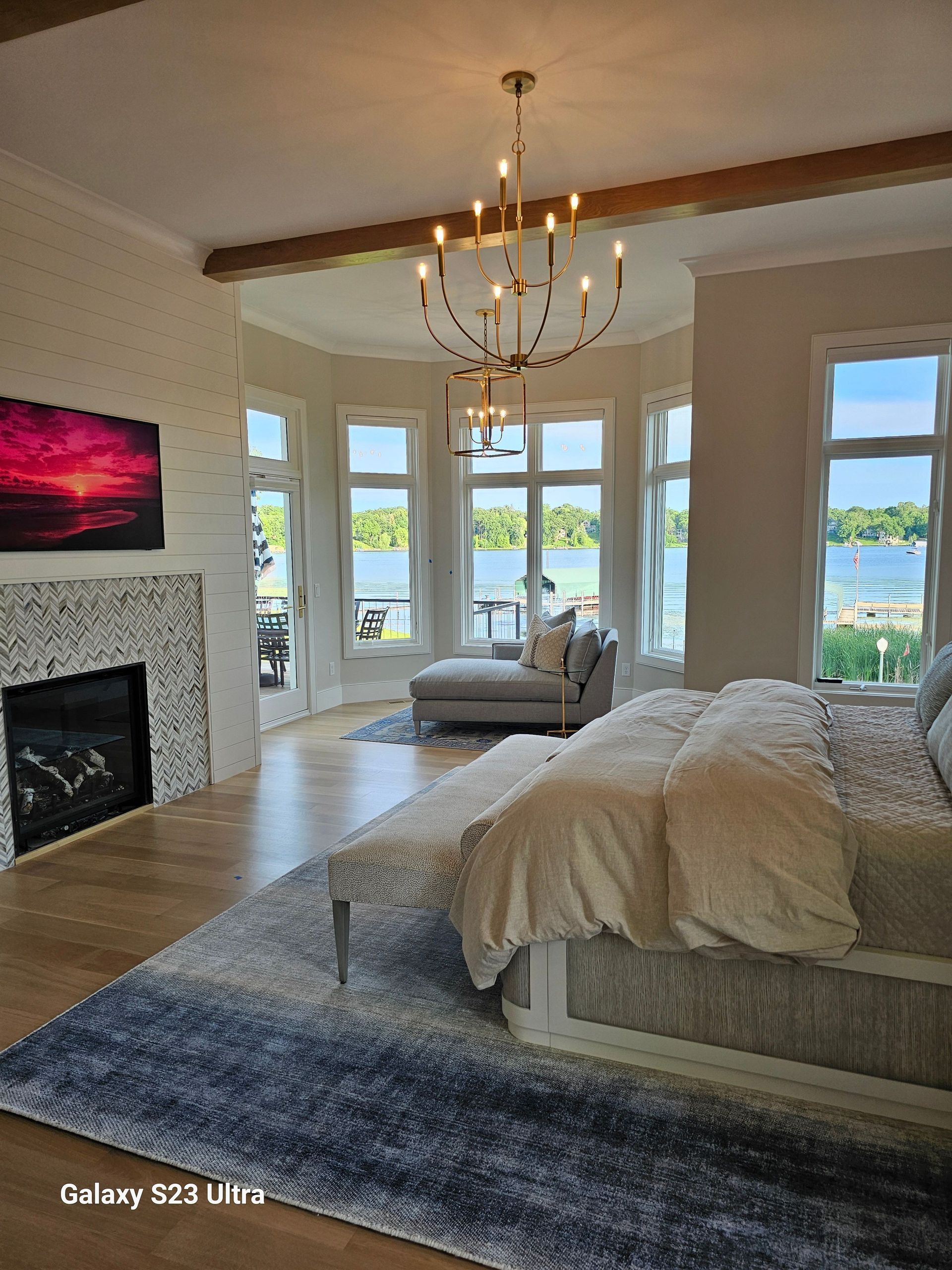 A bedroom with a large bed , fireplace , couch and chandelier.