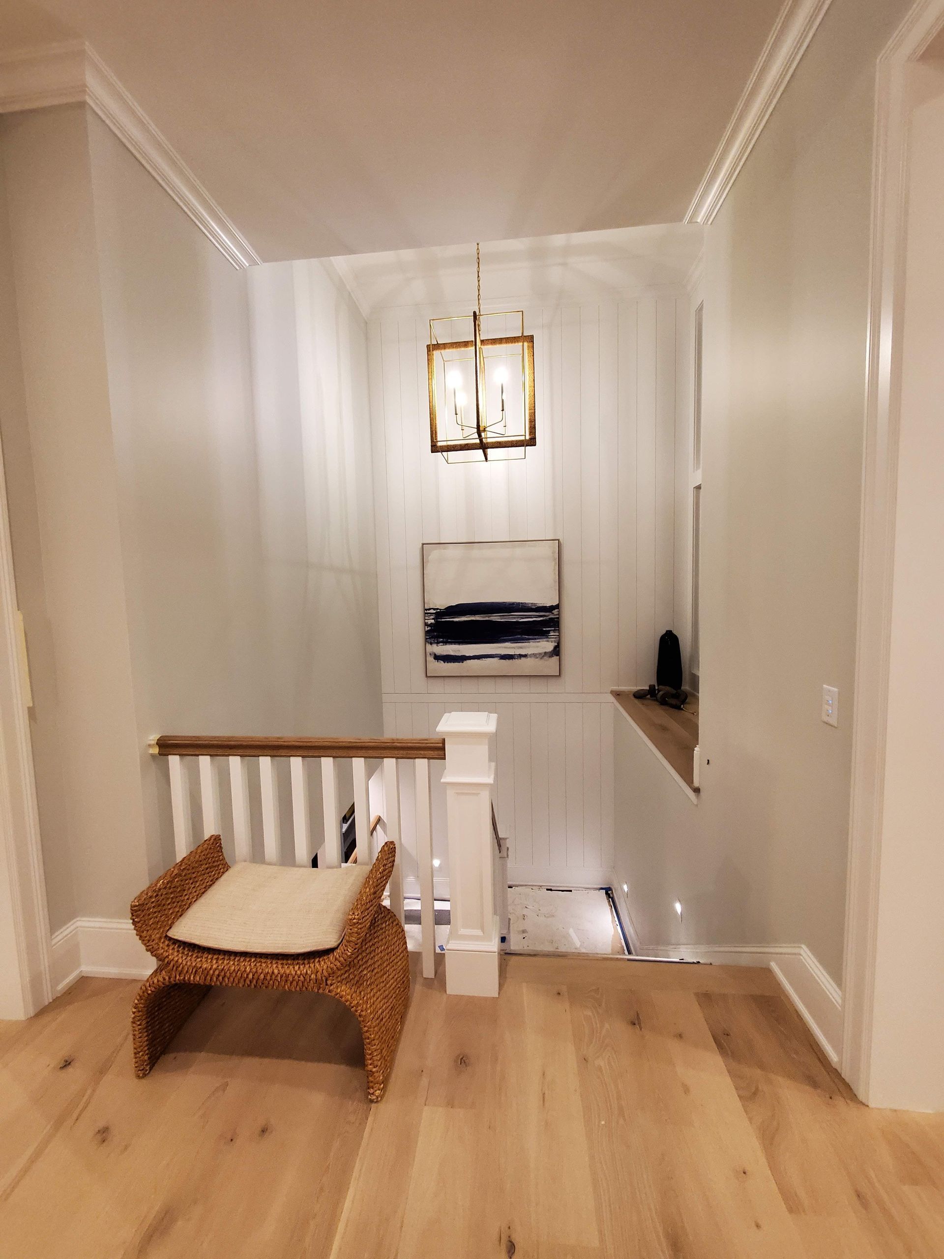 A hallway with a wicker chair and a chandelier hanging from the ceiling.
