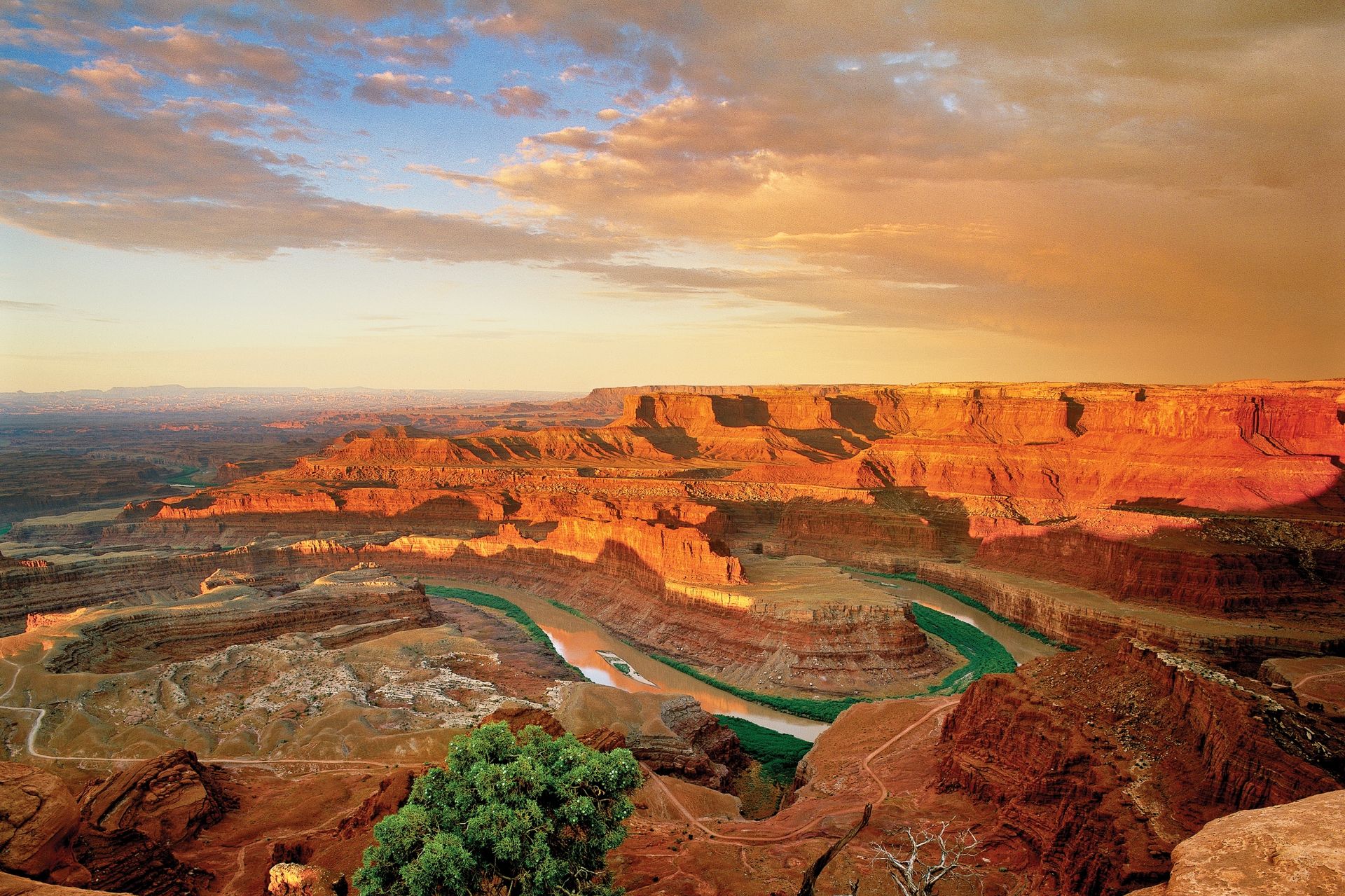Dramatic Overlook into Canyonlands National Park with a sunset casting orange light. The Colorado River winds through red rock formations.