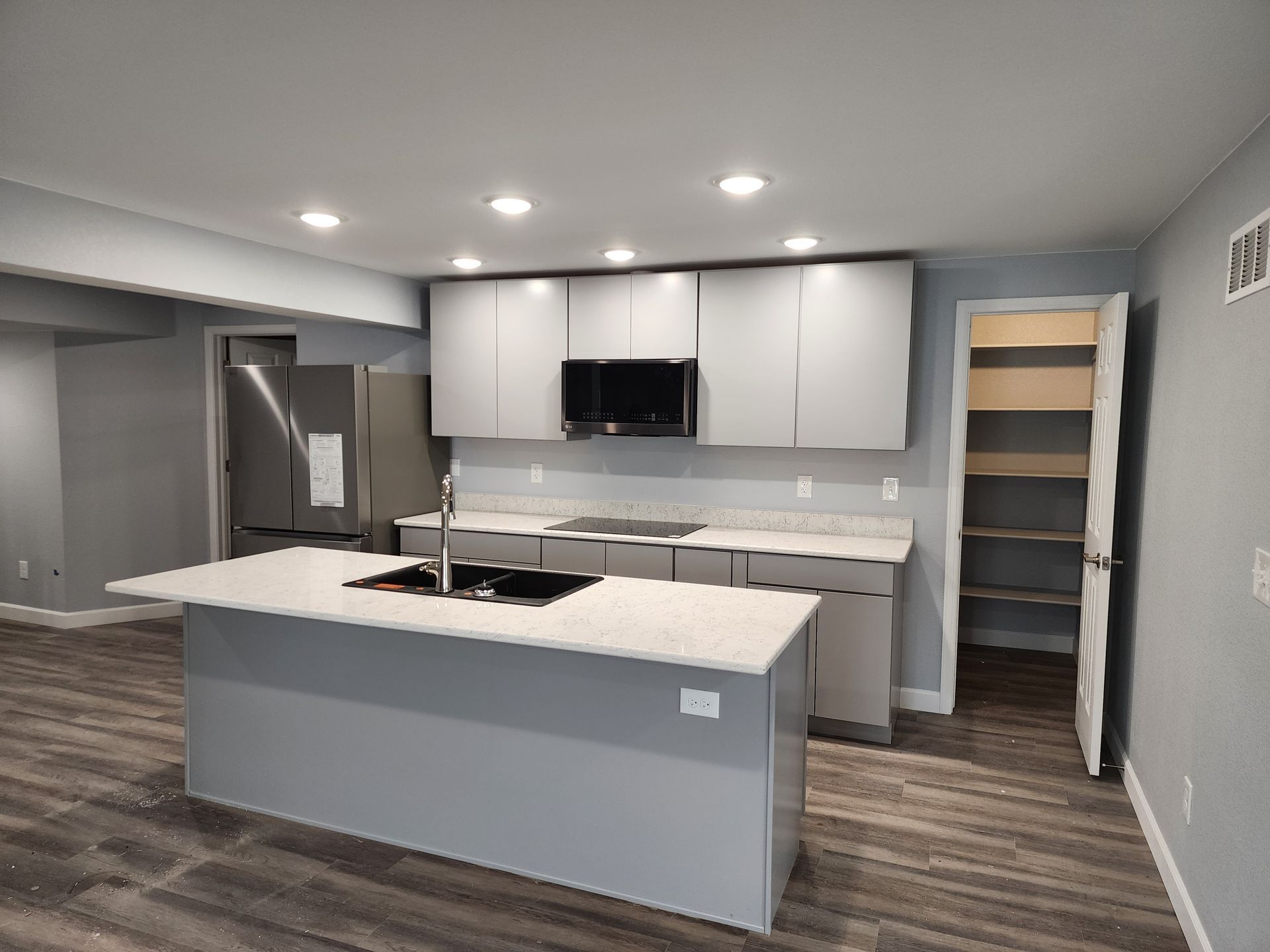 Modern kitchen with gray island, white cabinets, stainless range hood, and open pantry shelves