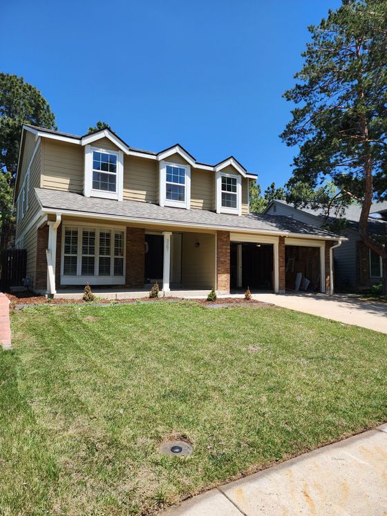 Two-story suburban house with stone facade, front lawn, and blue sky.