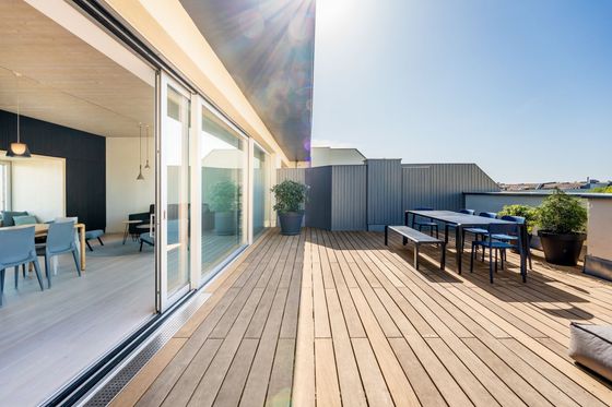 Sunny rooftop deck with wooden flooring, dining table, potted plants, and large sliding glass doors
