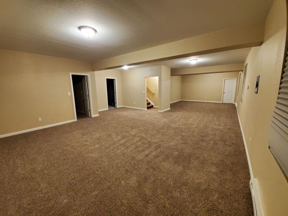 Empty beige carpeted living room with recessed ceiling light and open doorway to stairs in back