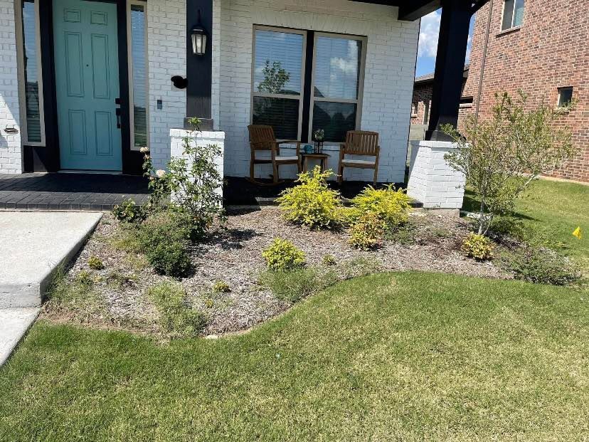 A house exterior with a turquoise door, white brick, and a small flower bed with green grass.