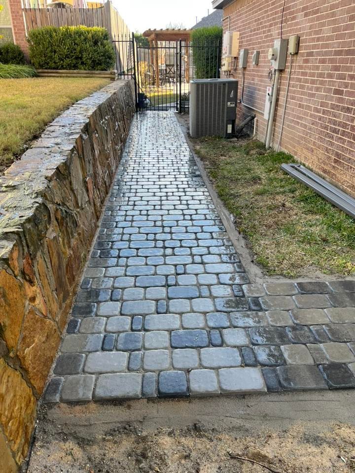 Brick pathway alongside a stone retaining wall and a brick building, leading to a gate.