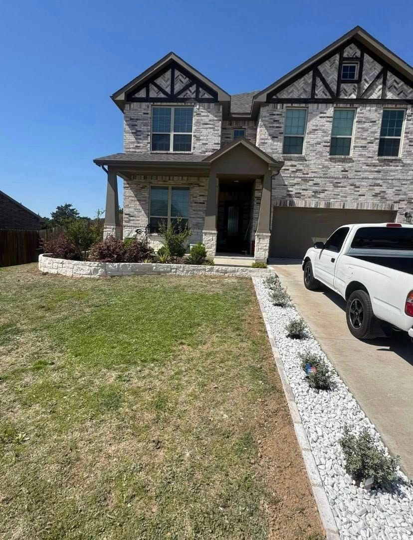 Two-story stone house with a white truck parked in the driveway. Landscaping in front.