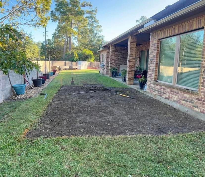 Backyard patio area with cleared dirt patch, surrounded by grass, next to a brick house.