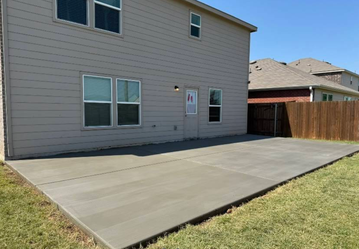 Backyard concrete patio next to a house with a door, windows, and a wooden fence.