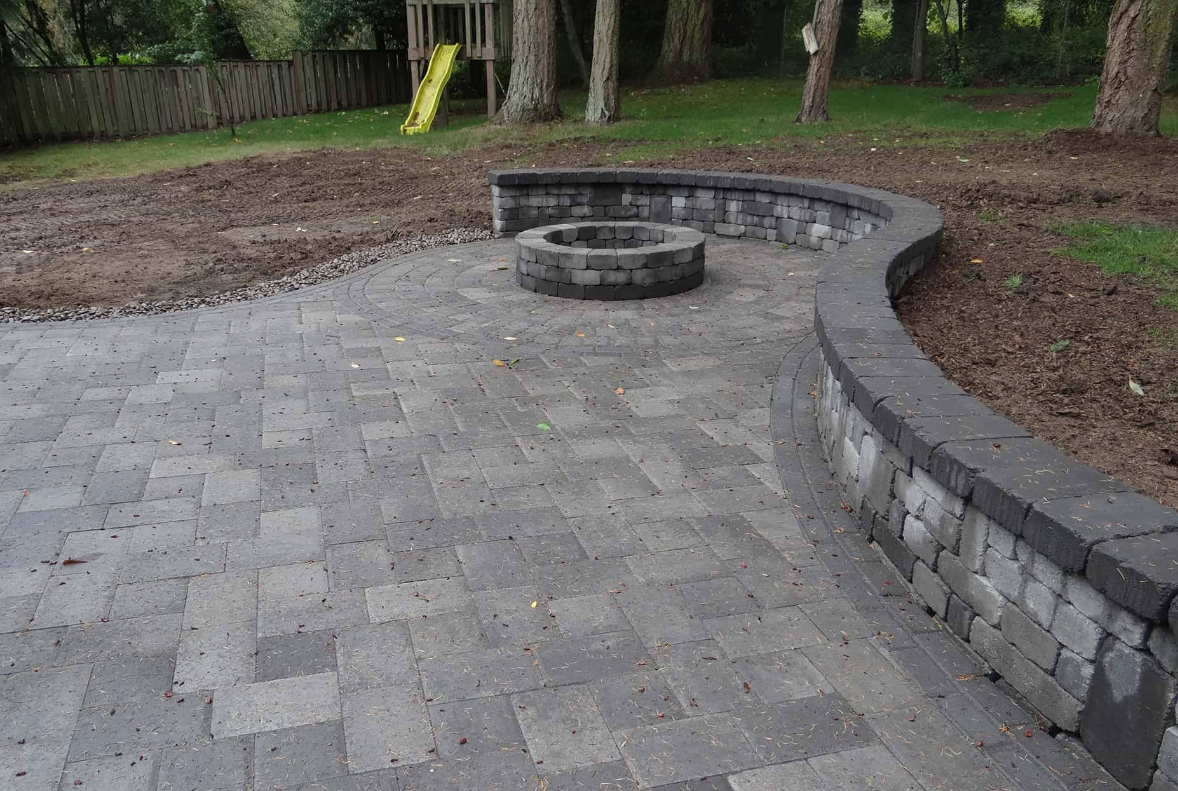 Paver patio with curved stone retaining wall, fire pit, and playground in the background.
