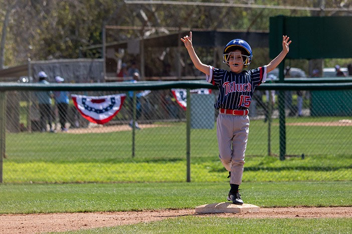 Boy in baseball uniform running, arms raised in the air after reaching home base.