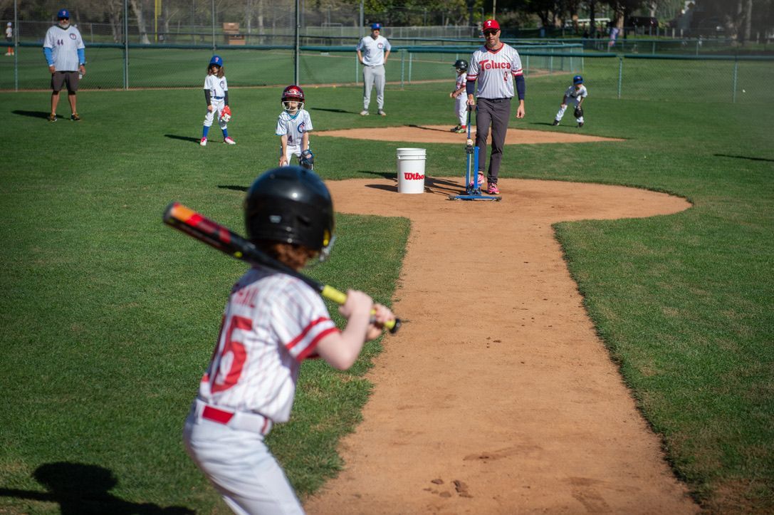 Youth baseball game: batter at the plate, teammates in the field, coach observing, sunny day.