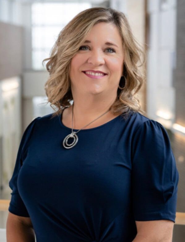 A woman in a blue shirt and necklace is smiling for the camera.