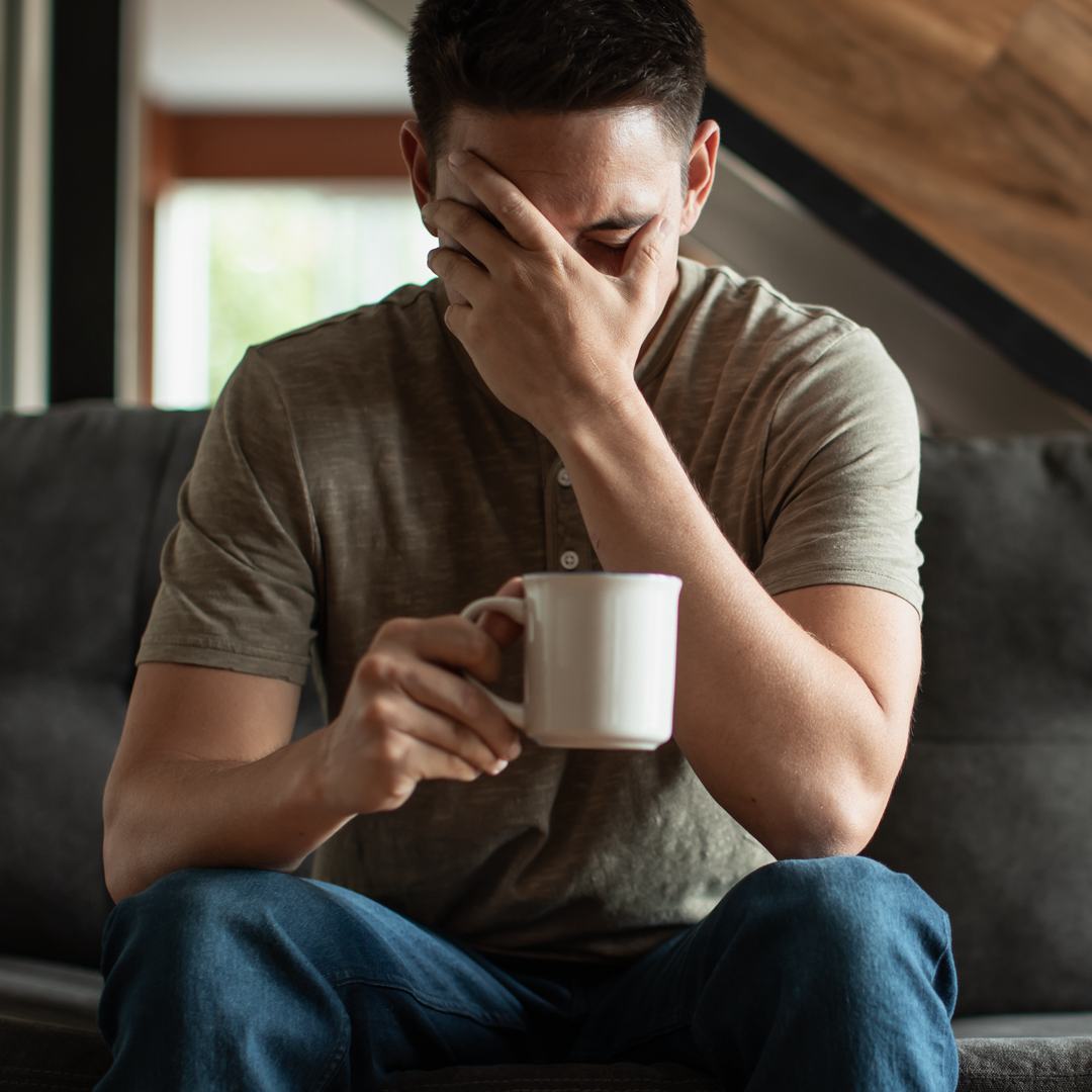 A man covering his face while holding a cup of coffee