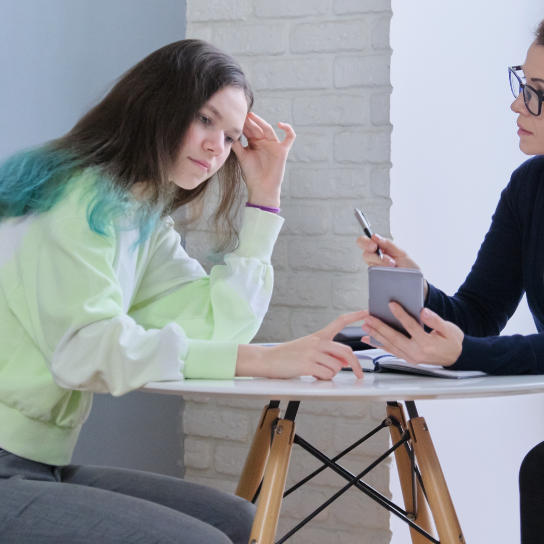 Two women are sitting at a table looking at a cell phone.