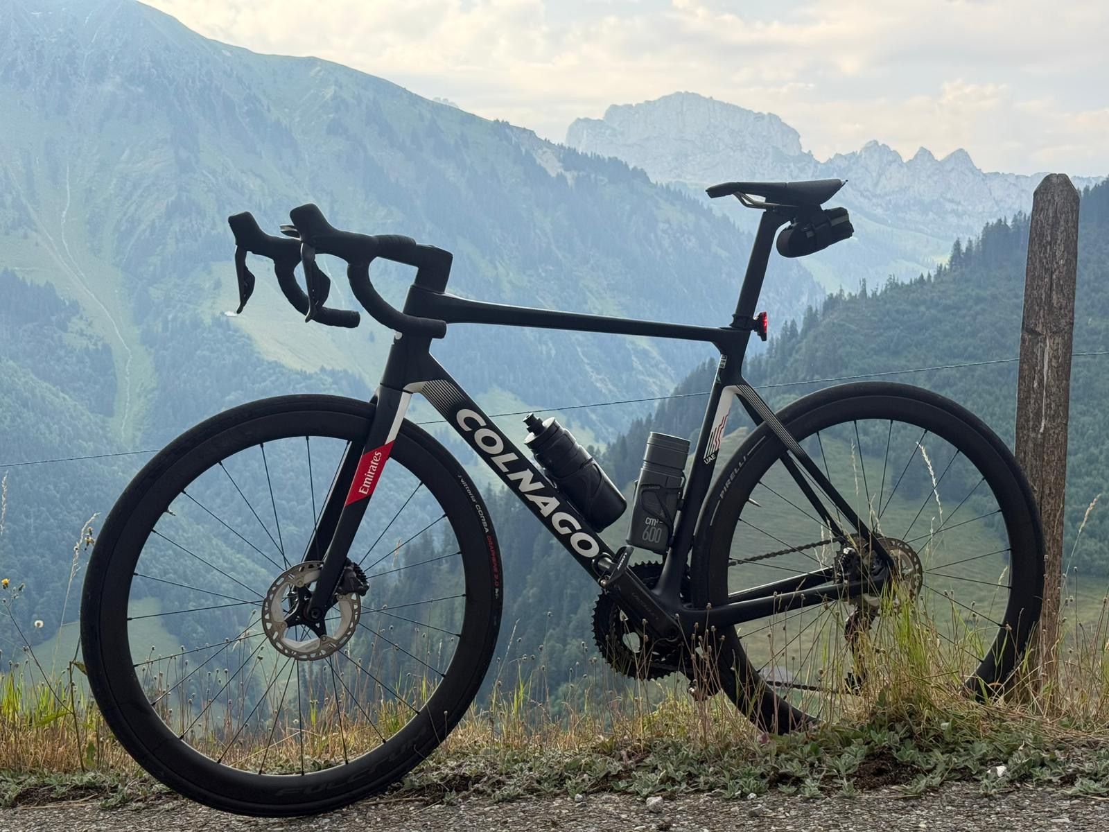 Vélo de route Colnago noir garé à flanc de colline, avec vue sur les montagnes en arrière-plan.
