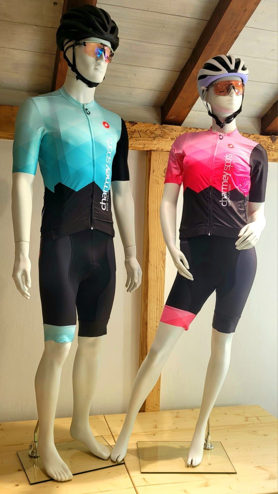 Deux mannequins en tenue de cyclisme, l'un bleu/noir et l'autre rose/noir, portant casques et lunettes de soleil.