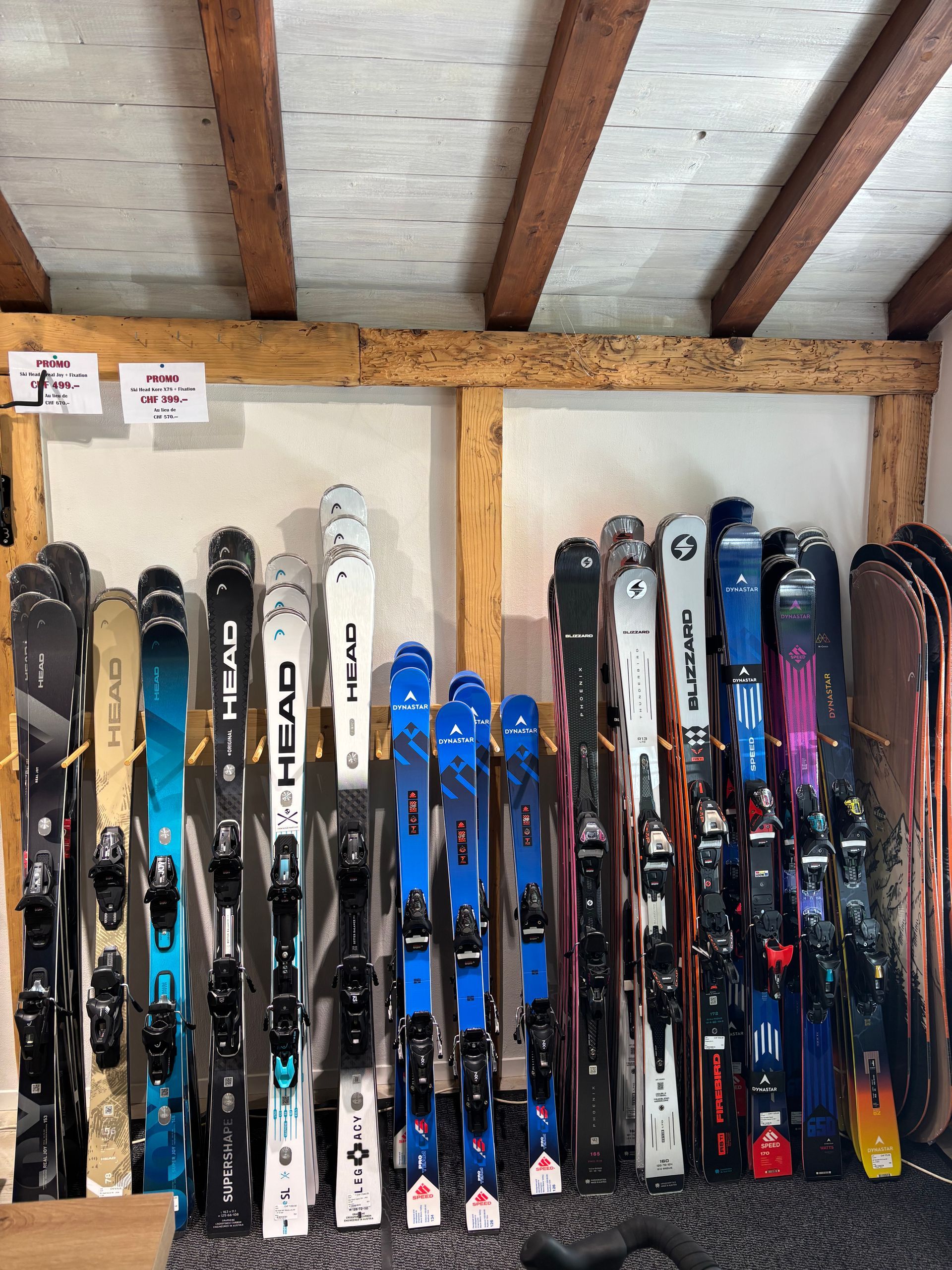 Rangée de skis de différents types montés sur un cadre en bois, à l'intérieur.