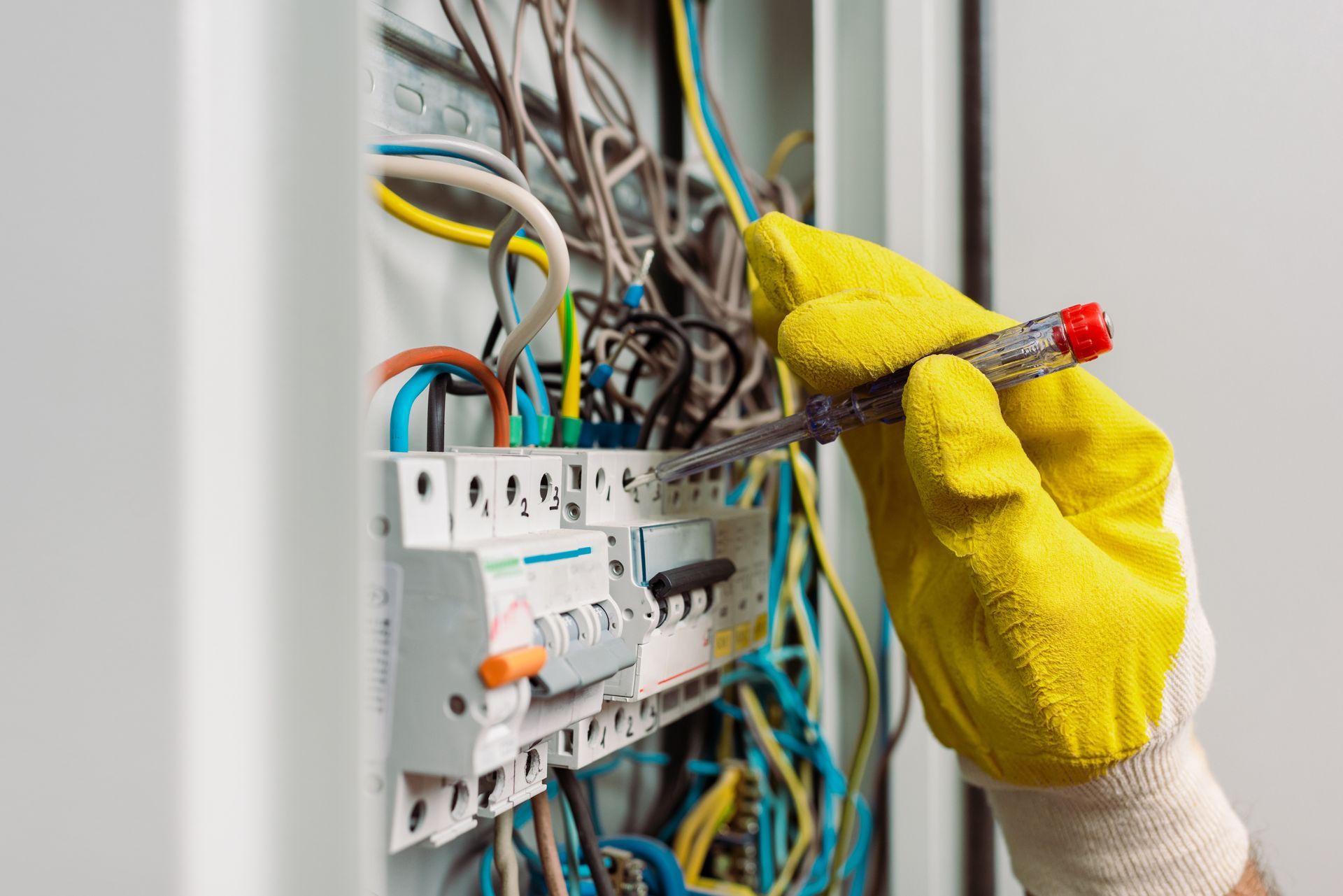 Gloved hand using a screwdriver to adjust wiring inside an electrical breaker panel.