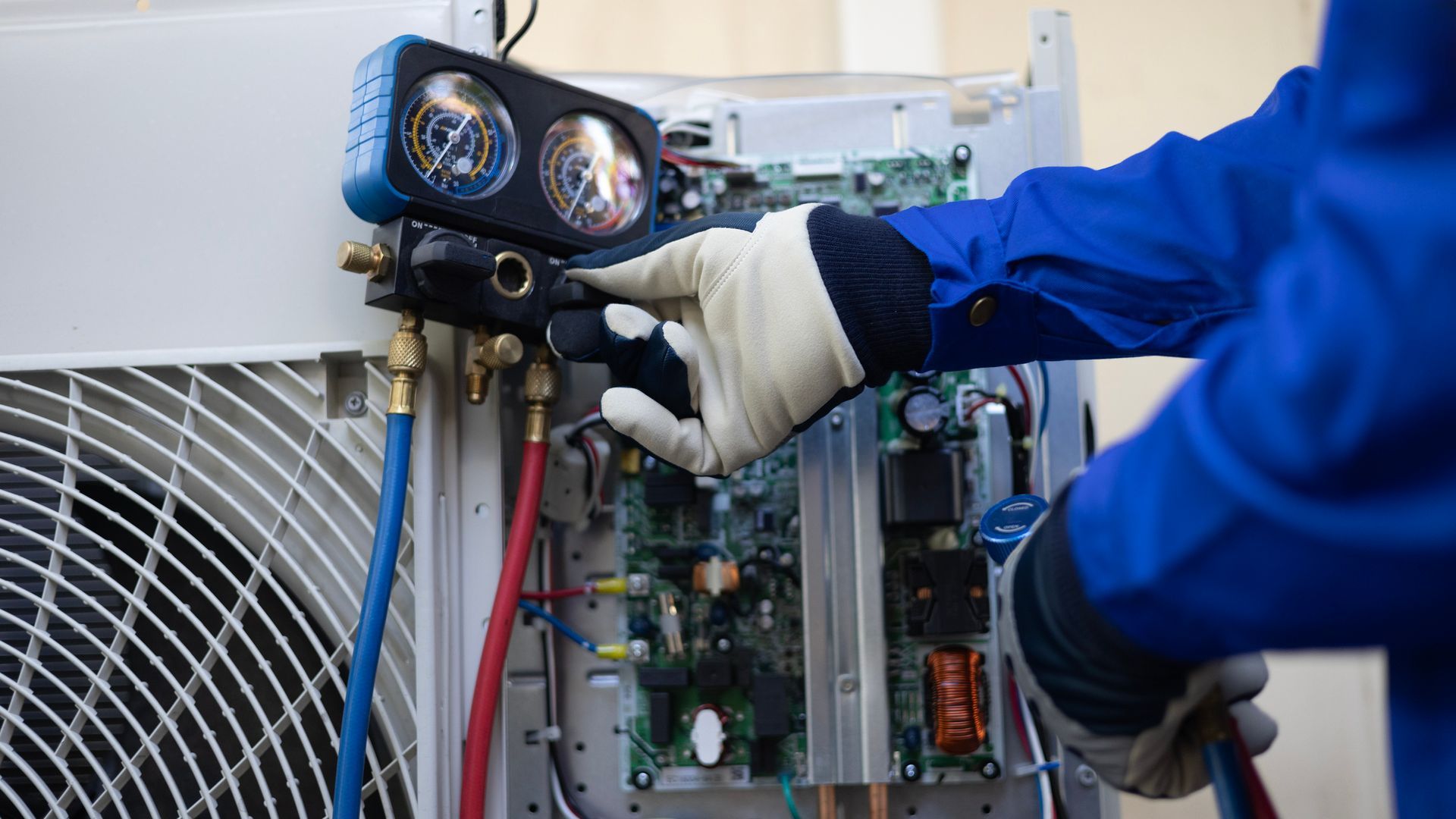 Person in blue coveralls attaching gauges to an air conditioner unit.