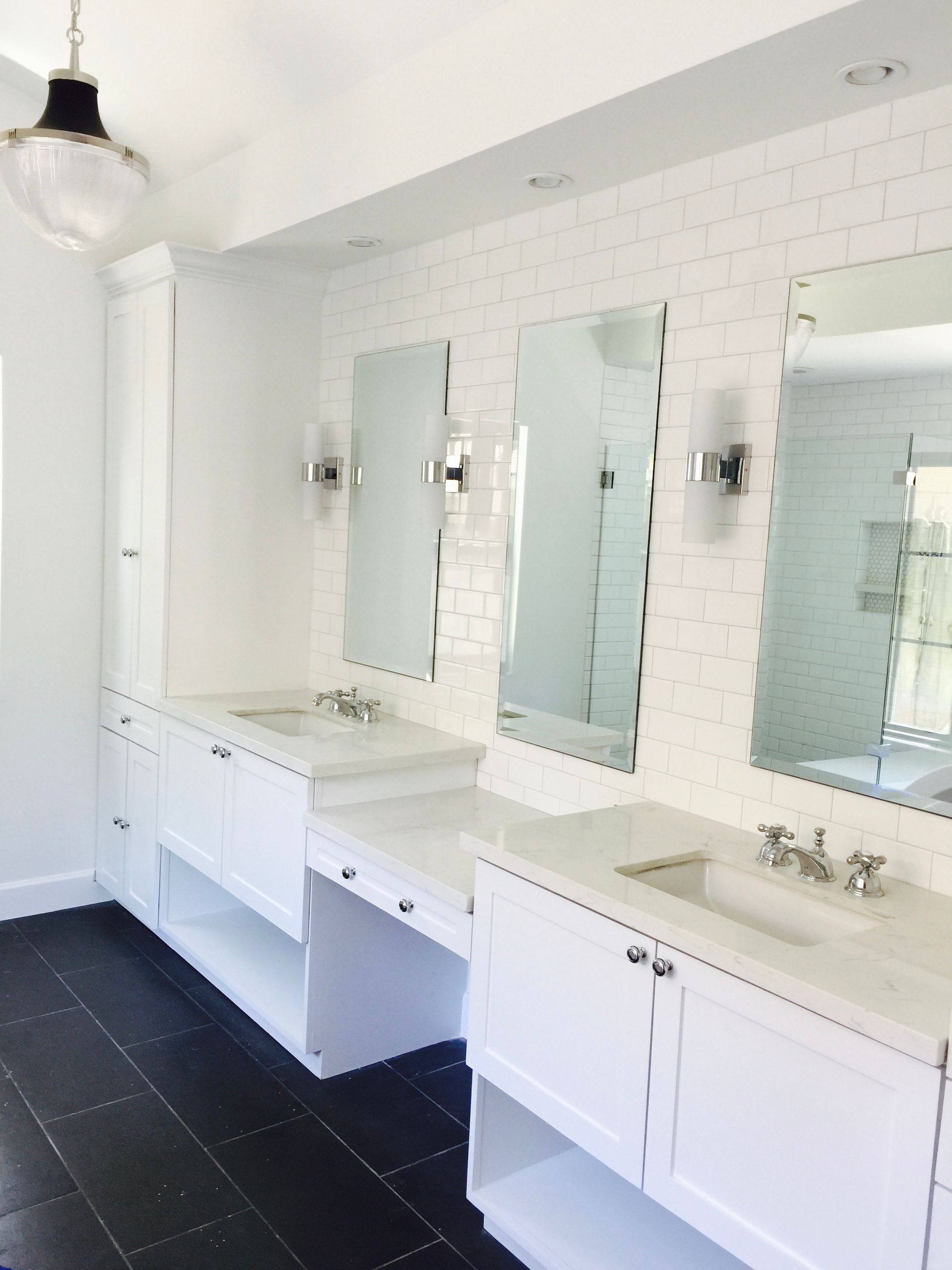White bathroom with three sinks, mirrors, and black flooring.