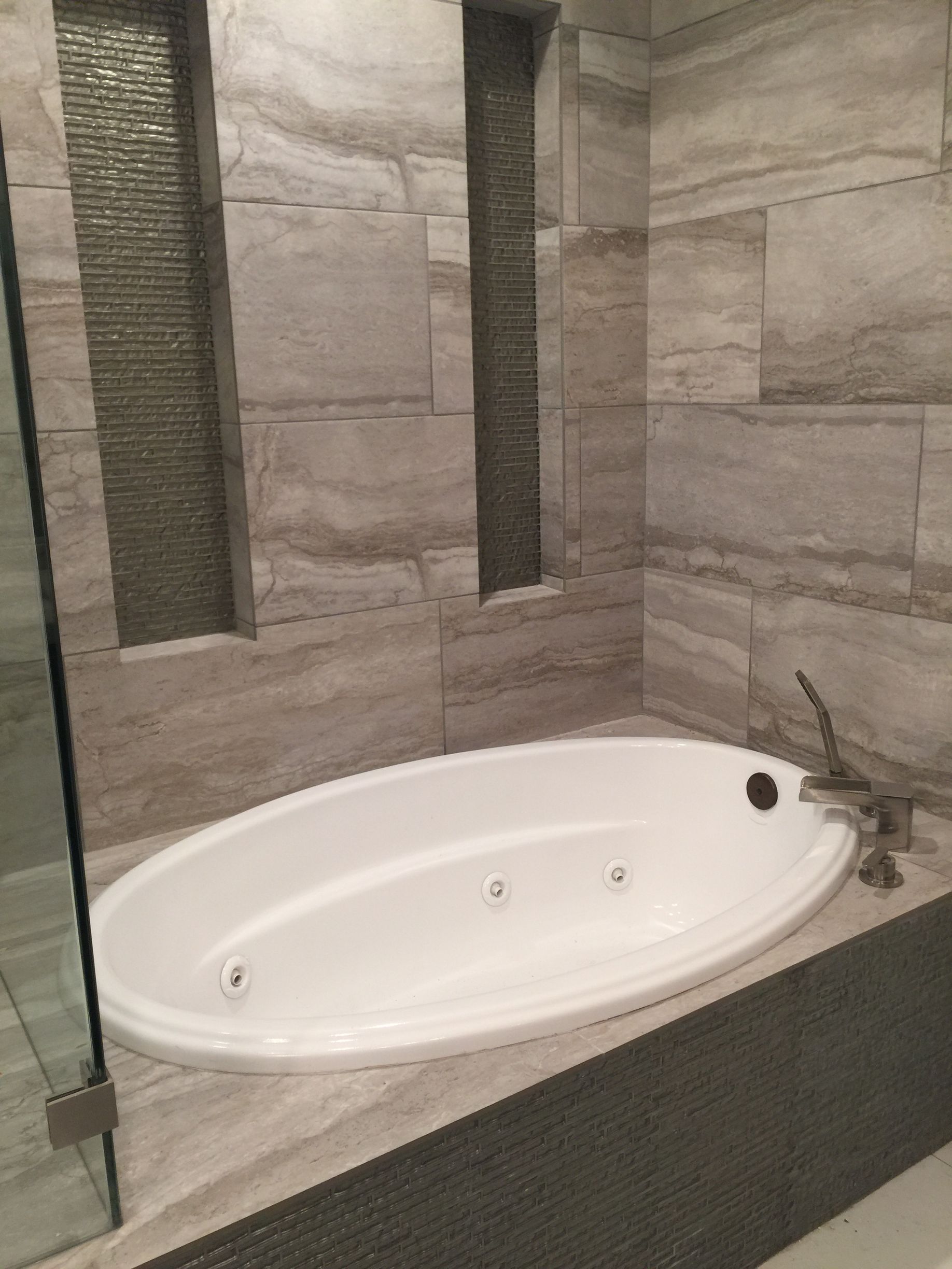 Oval jacuzzi tub in a bathroom with textured gray tile walls, glass shower door.