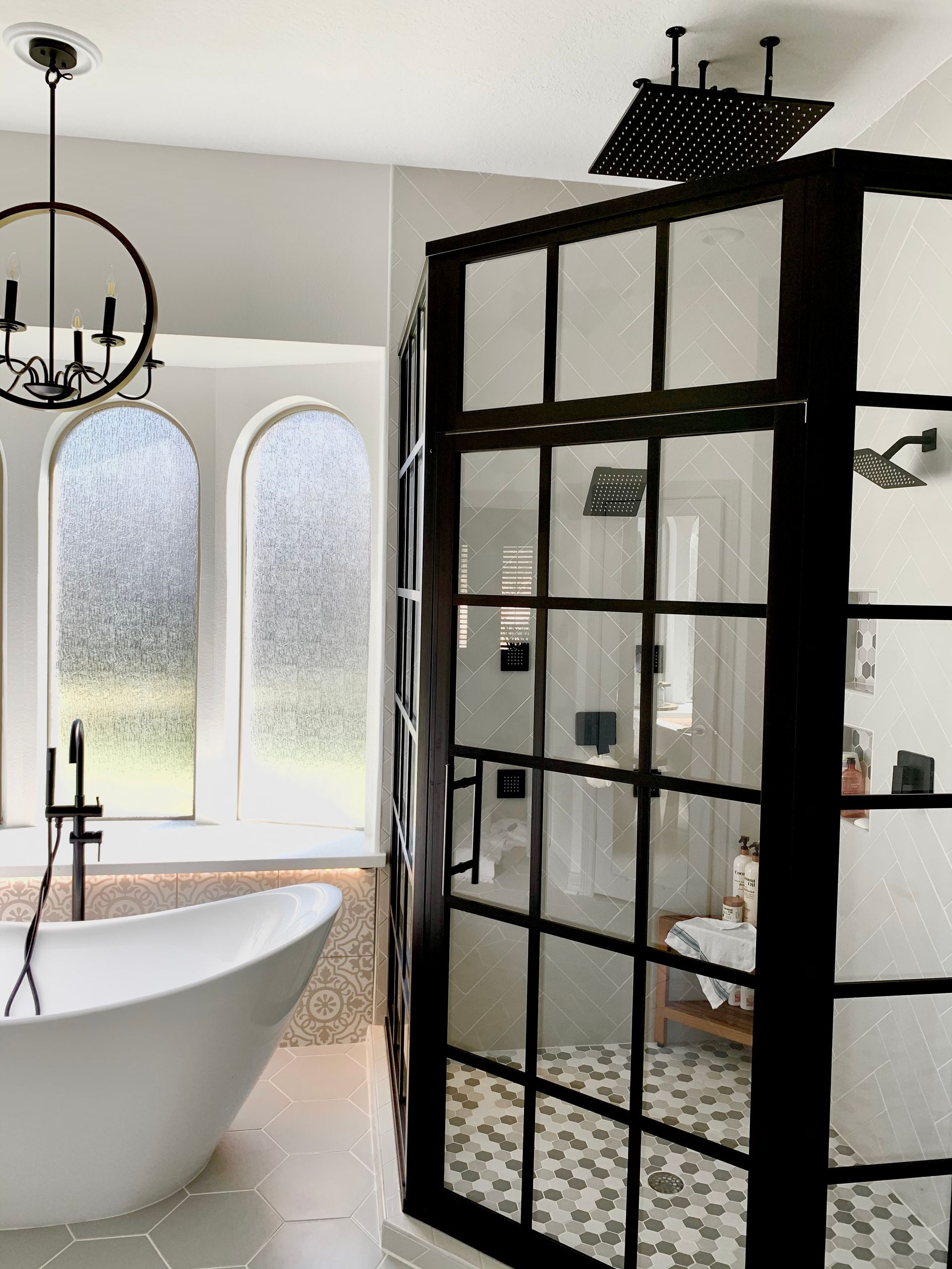 Modern bathroom with a glass-enclosed shower, freestanding tub, and a decorative chandelier.