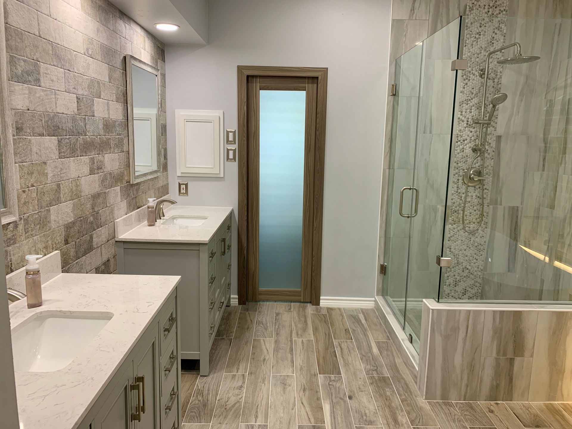 Bathroom with two sinks, stone tile walls, glass shower, and frosted glass door.