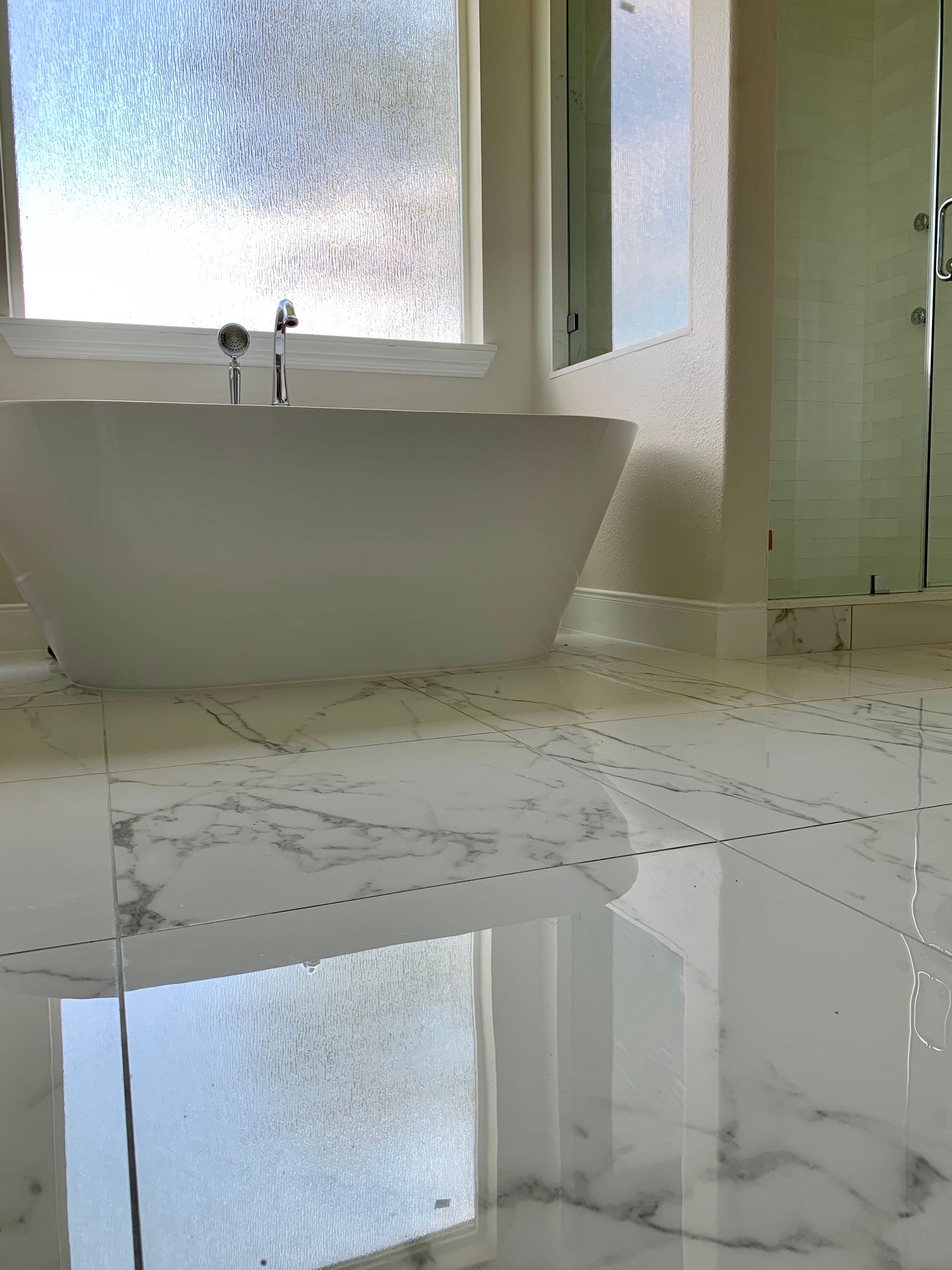 White bathtub in a modern bathroom with marble floors and a window.