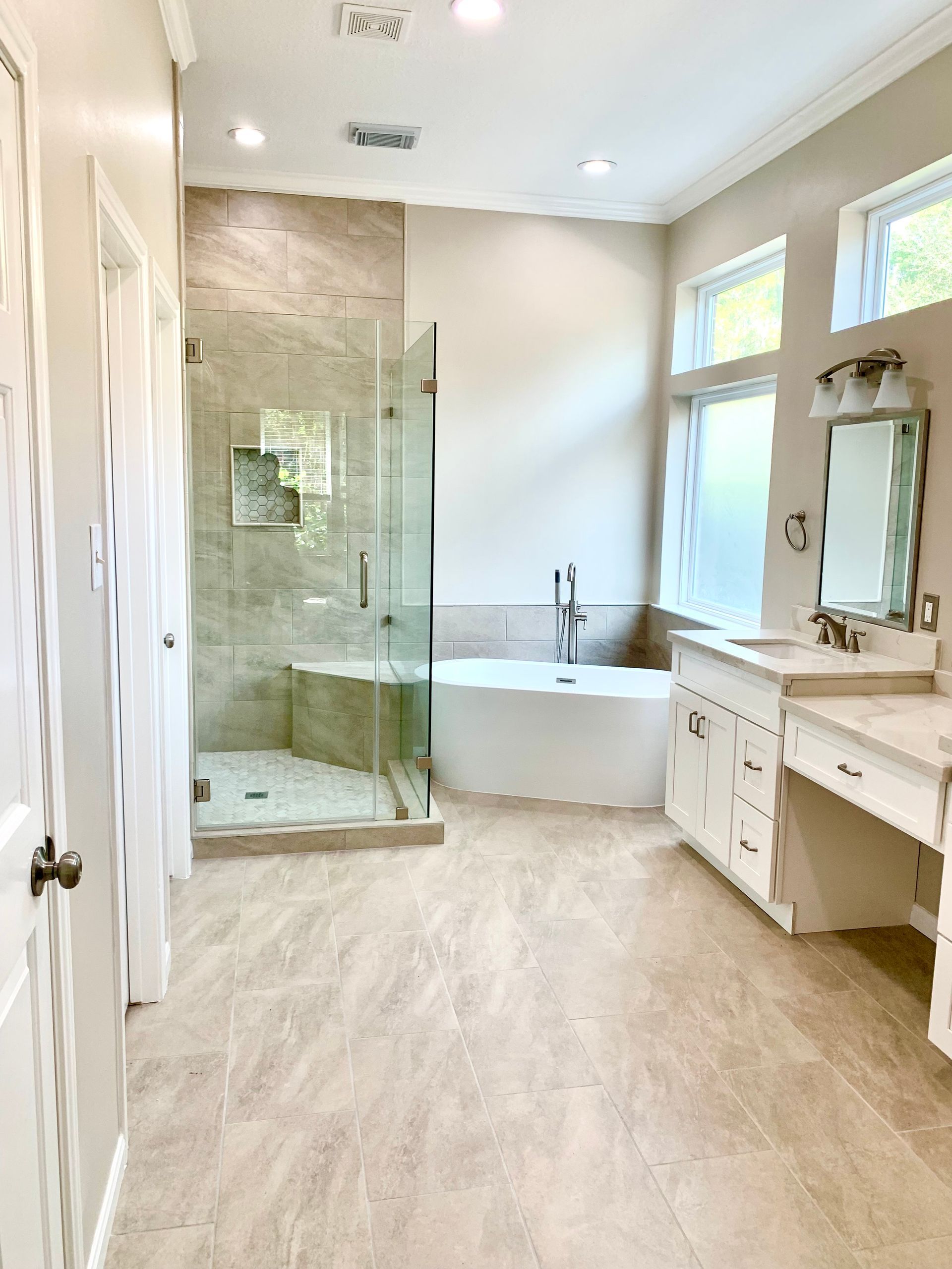 Spacious, light-colored bathroom with shower, tub, vanity, and large windows.