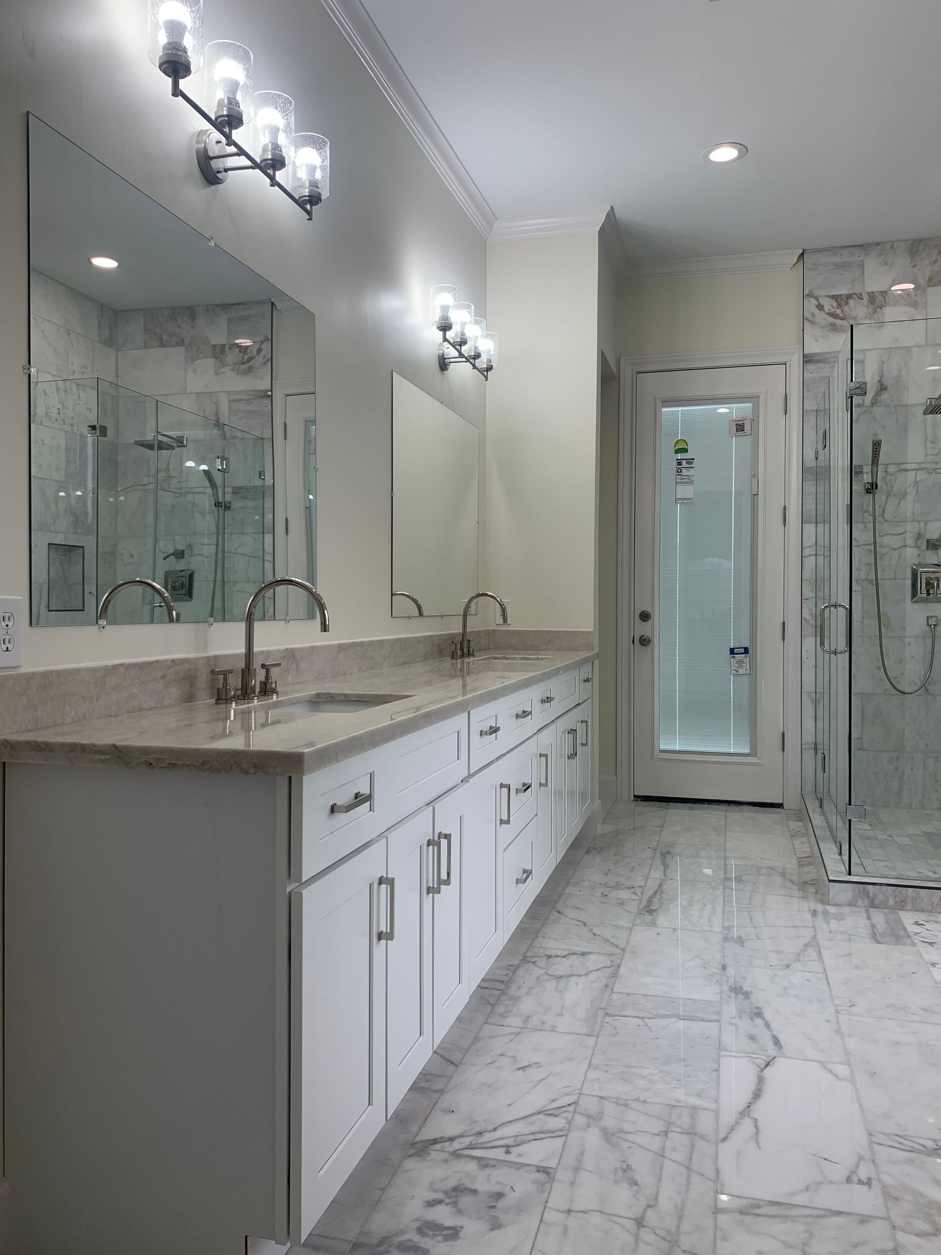 Brightly lit modern bathroom with marble floor, white vanity with two sinks, and a glass shower.