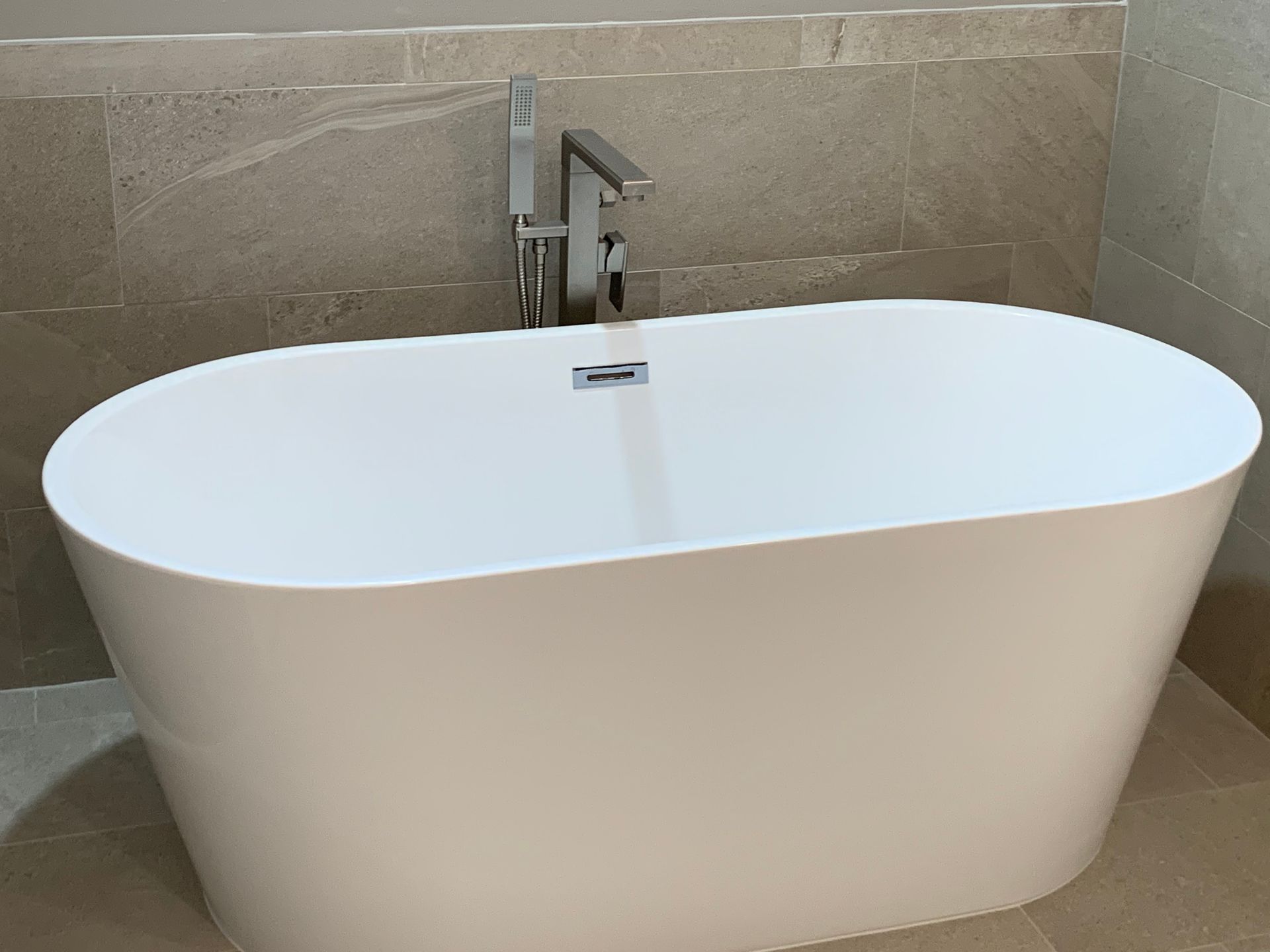 White freestanding bathtub with silver faucet, set against tan tiled wall.