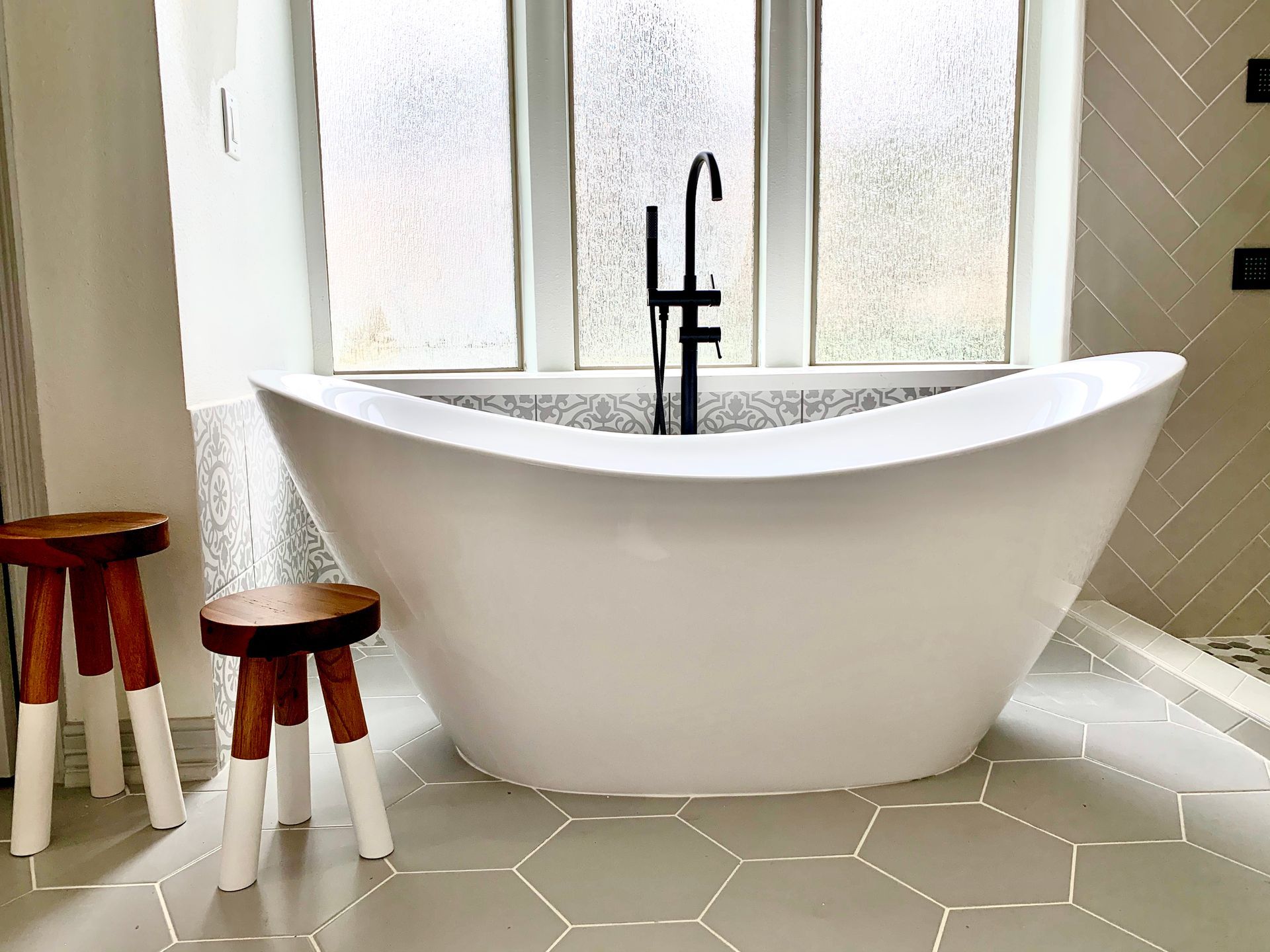 Freestanding white bathtub with black faucet, flanked by two wooden stools.