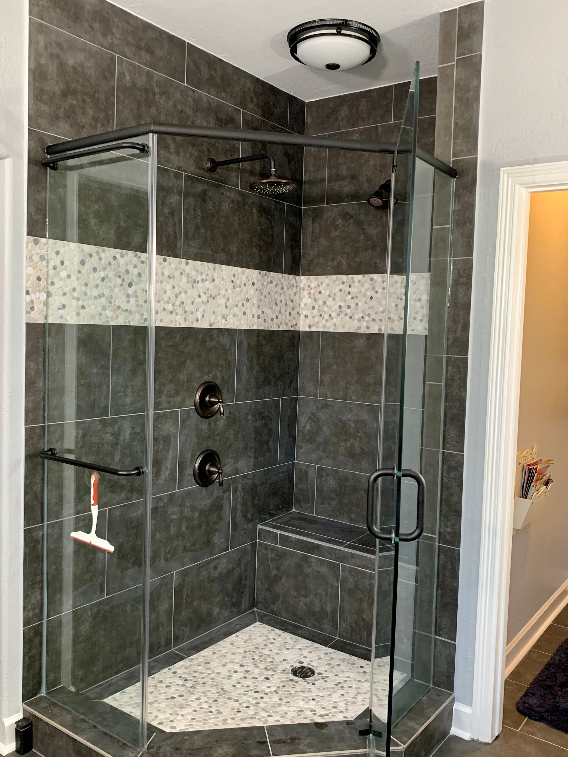 Corner shower with gray tile, glass door, and white pebble floor.
