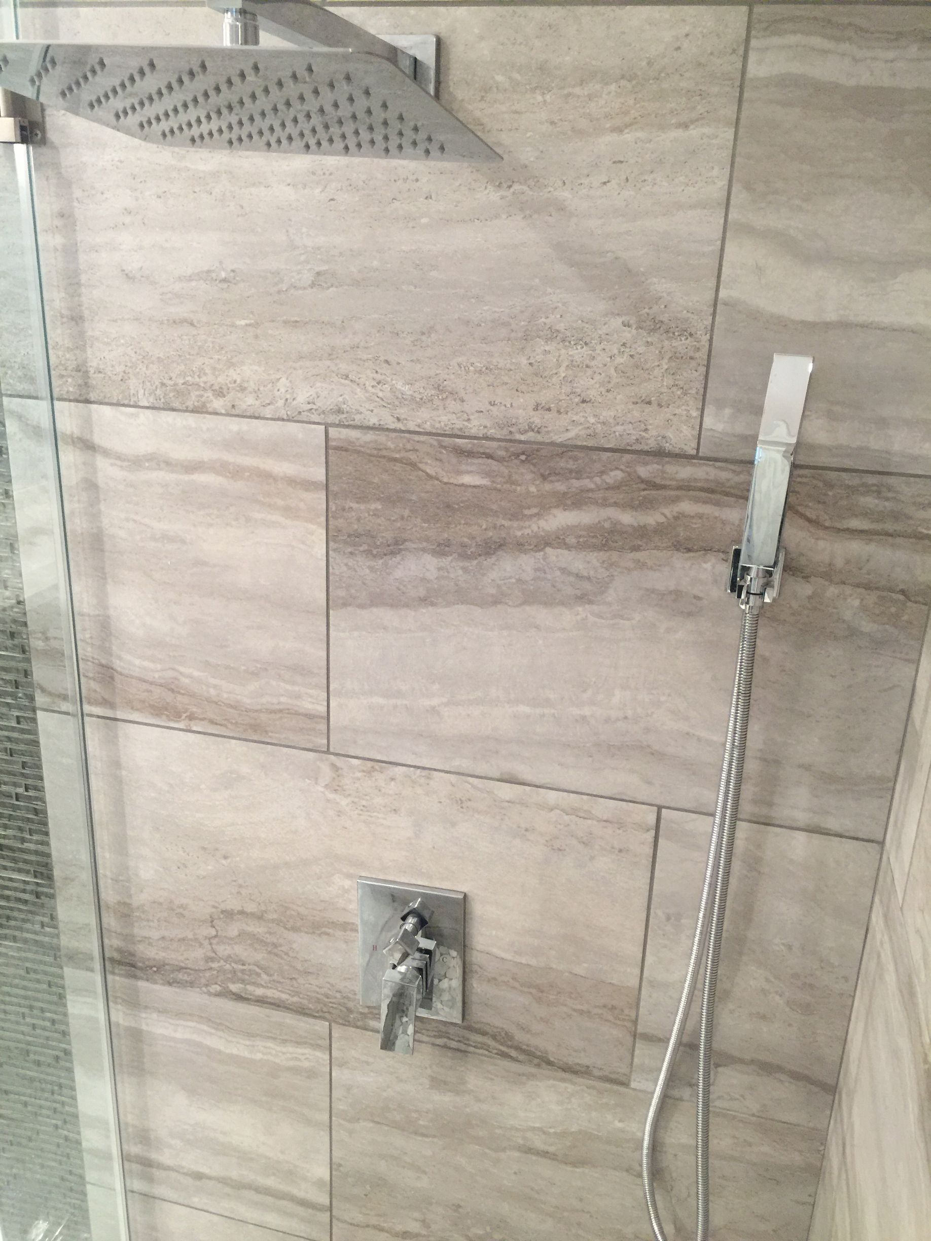 Shower with large square showerhead, handheld sprayer, and tiled walls.