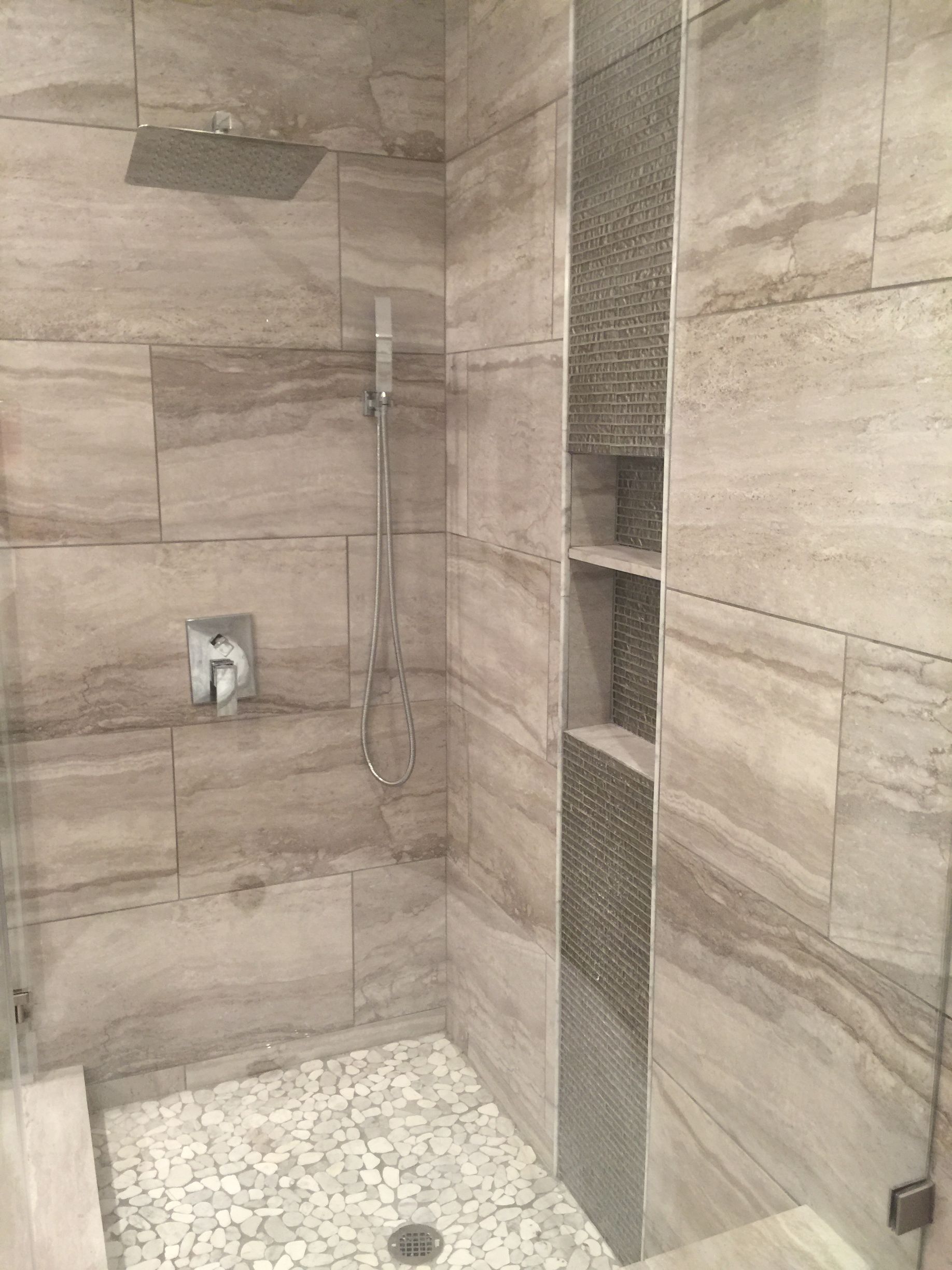 Shower with stone tile walls, pebble floor, and recessed shelf.