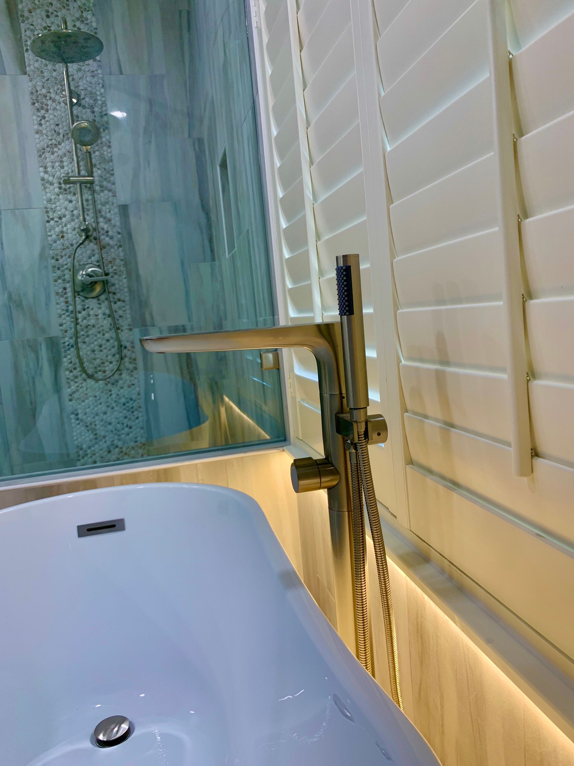 Bathtub with gold faucet, shower, and white shutters.