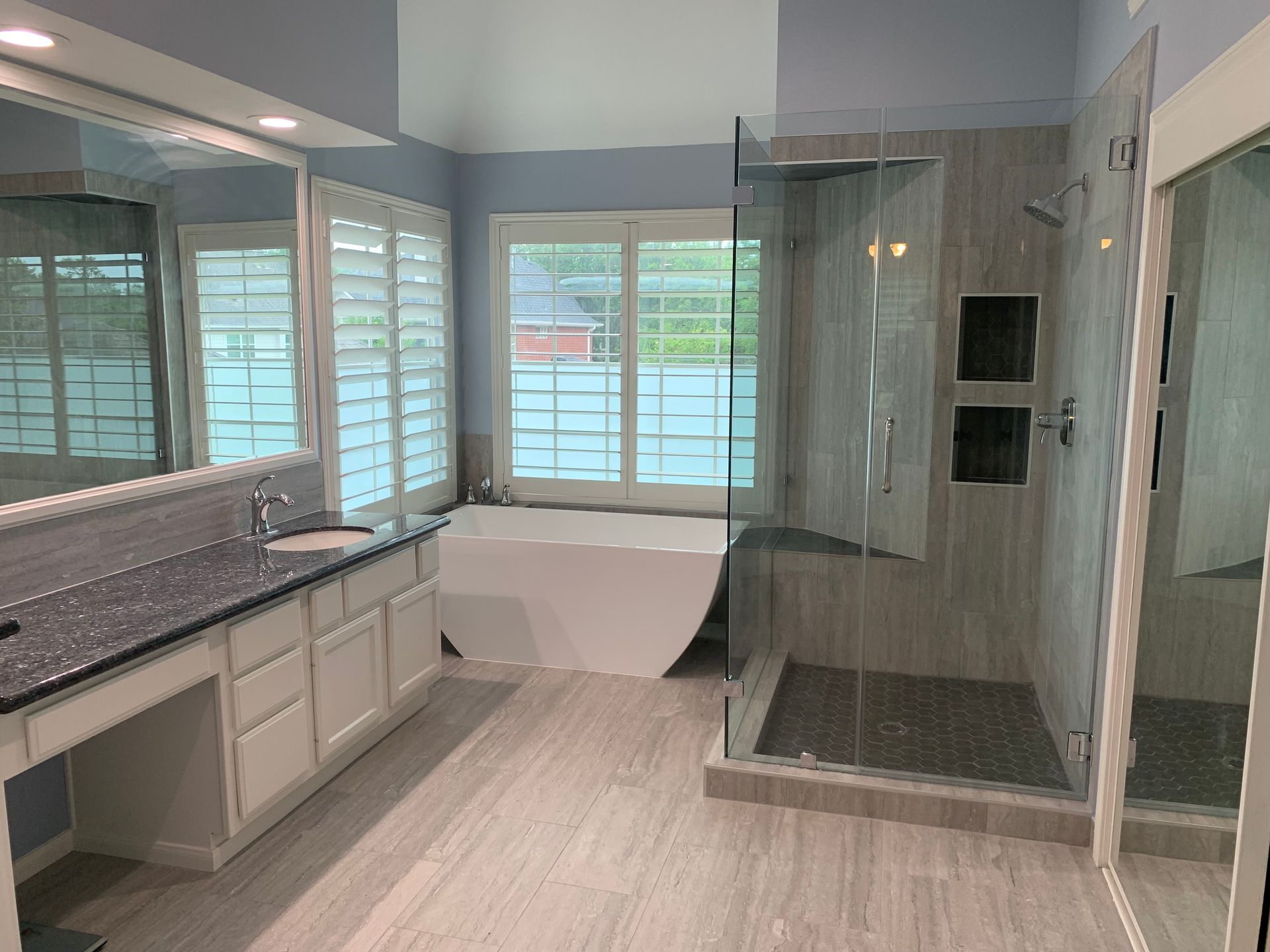 Bathroom with large vanity, soaking tub, glass shower, and shuttered window.