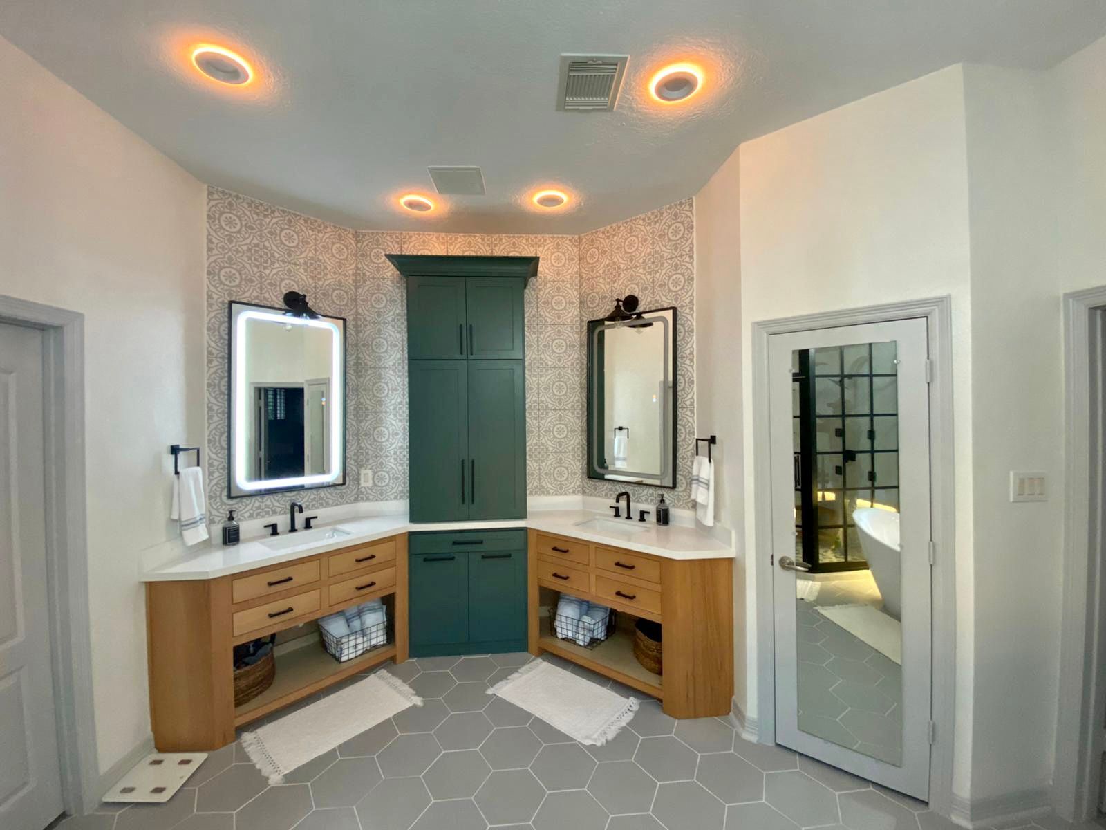A modern bathroom with light wood vanities, green cabinet, and hexagon tile floor.