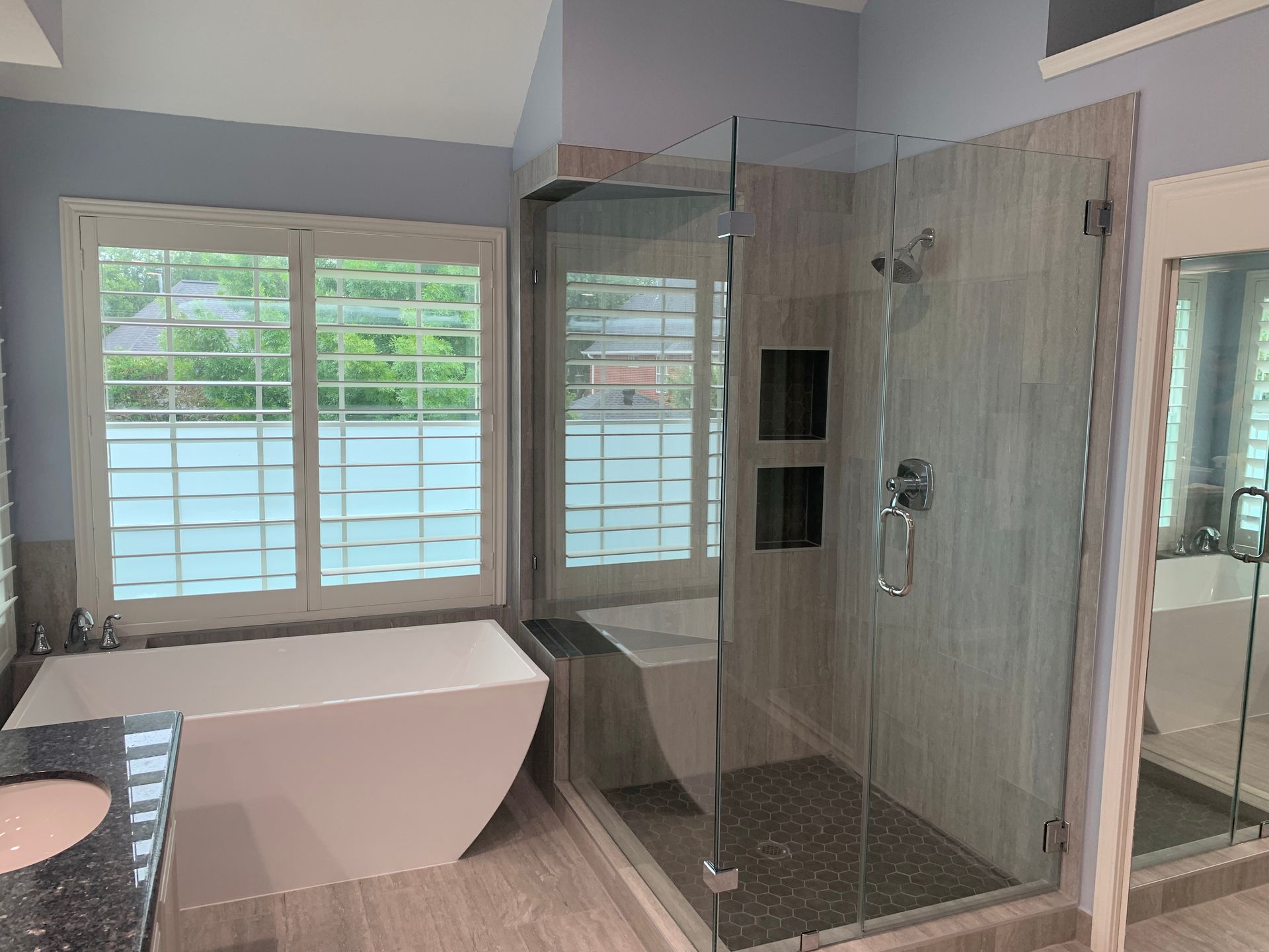 Bathroom with a modern white tub, glass shower, and shuttered windows.