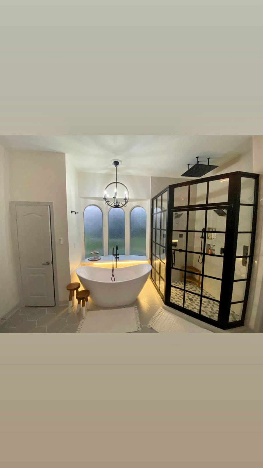 Bathroom with a freestanding tub, large shower enclosure, and arched window.