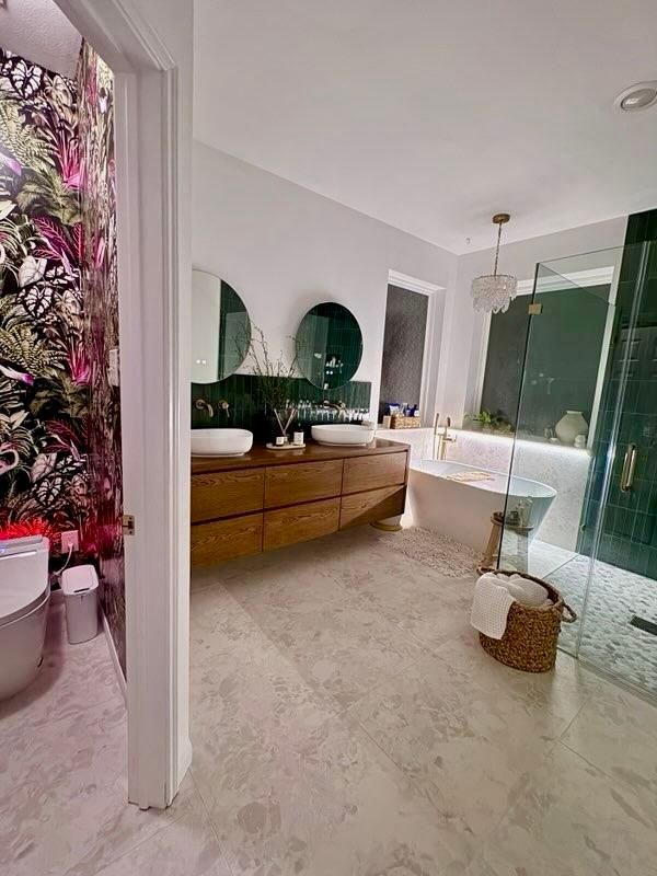 Bathroom with wooden vanity, round mirrors, soaking tub, and floral wallpaper.