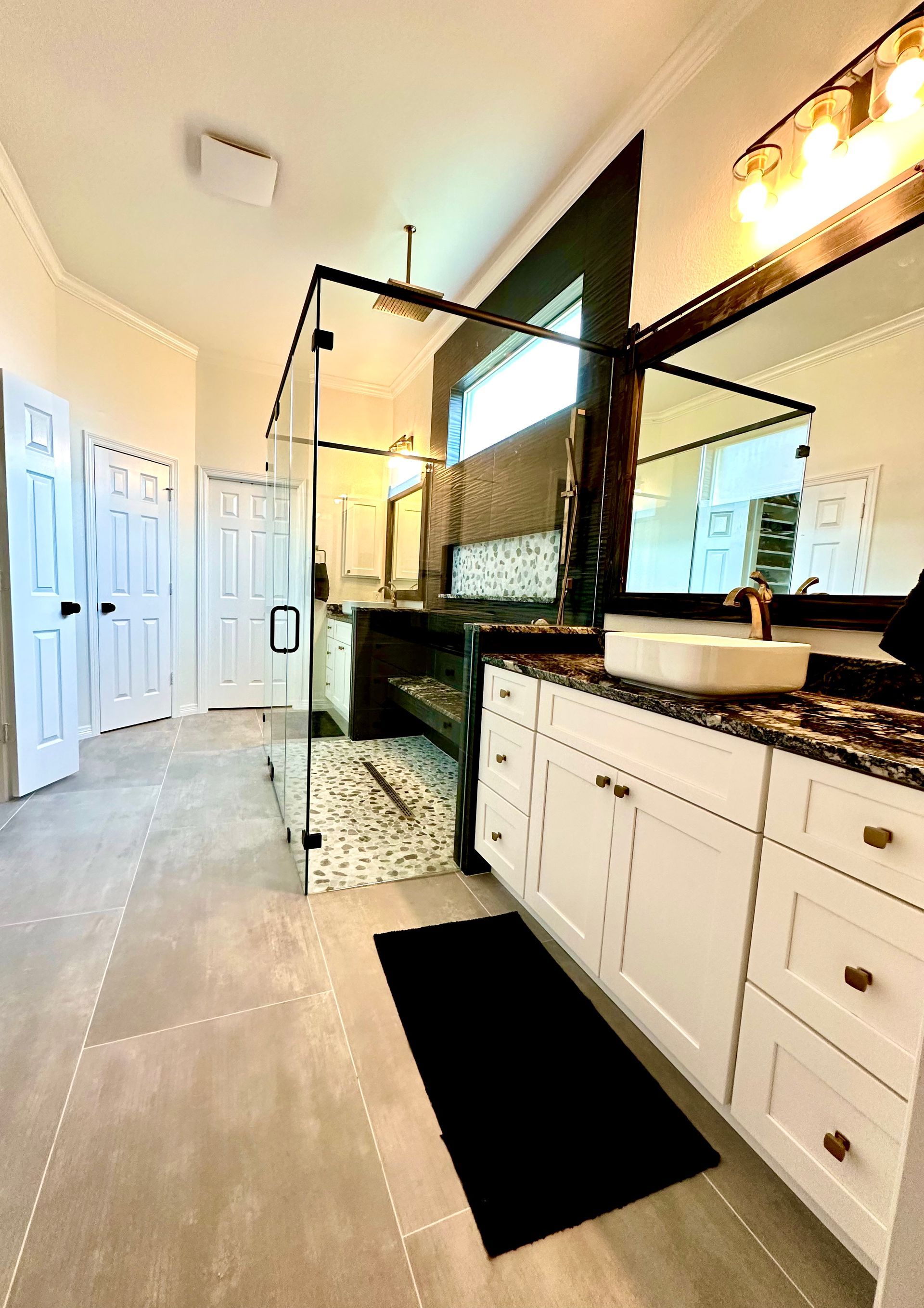 Modern bathroom with white cabinets, glass shower, and gray floor tiles.