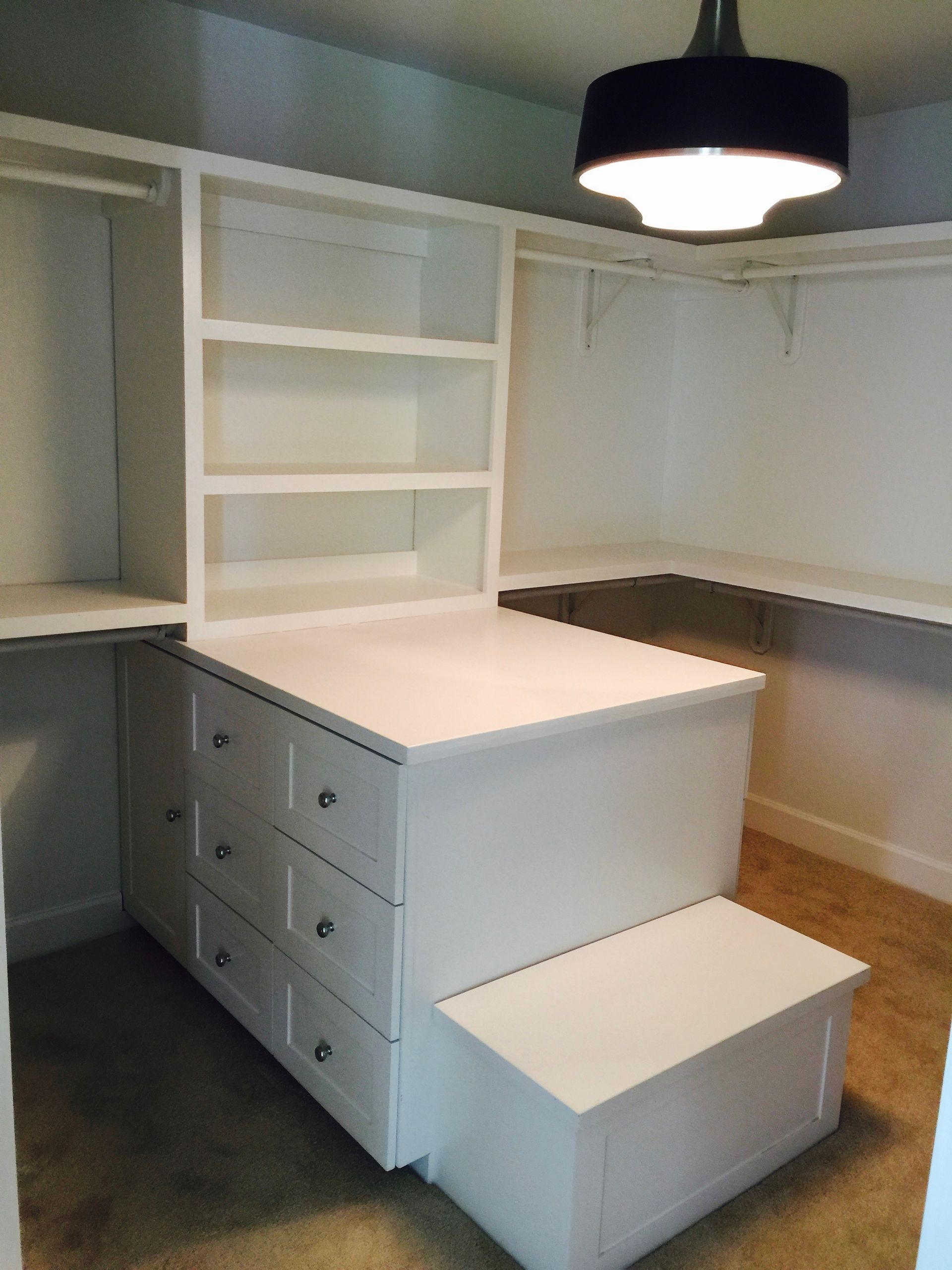 White closet with drawers, shelves, and a step, lit by a black pendant light.