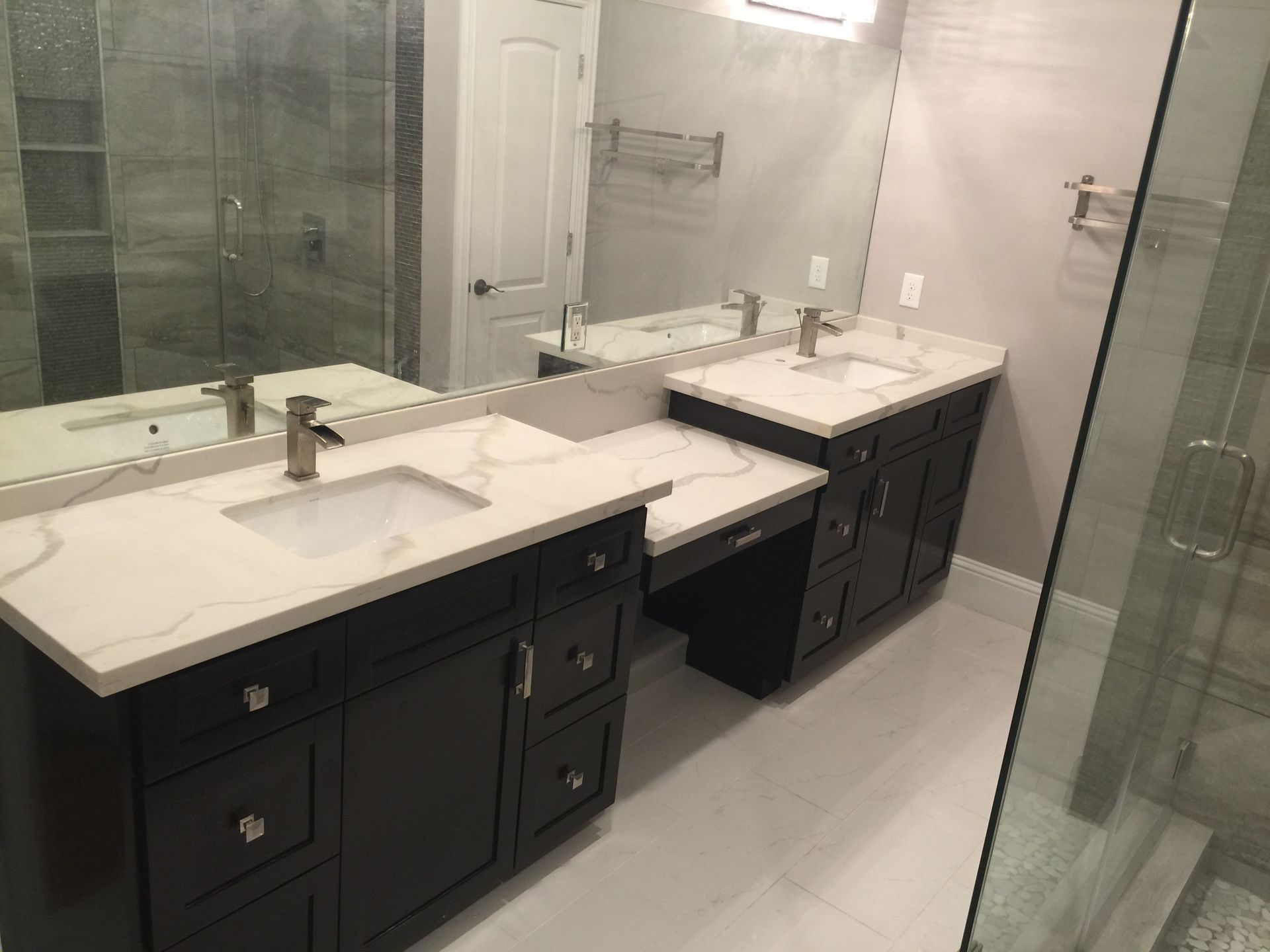 Dark brown double vanity with white countertops, large mirror, and glass shower in bathroom.