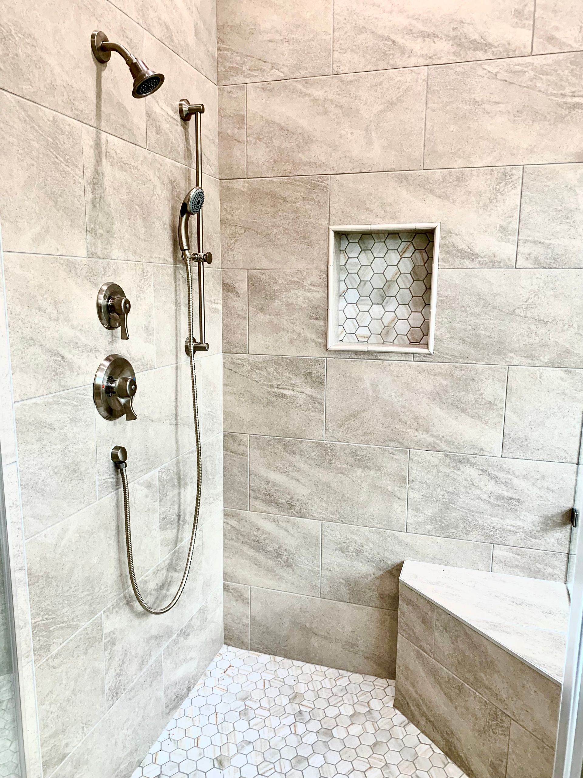 Shower stall with light gray stone tiles, pebble floor, built-in bench, and shower fixtures.