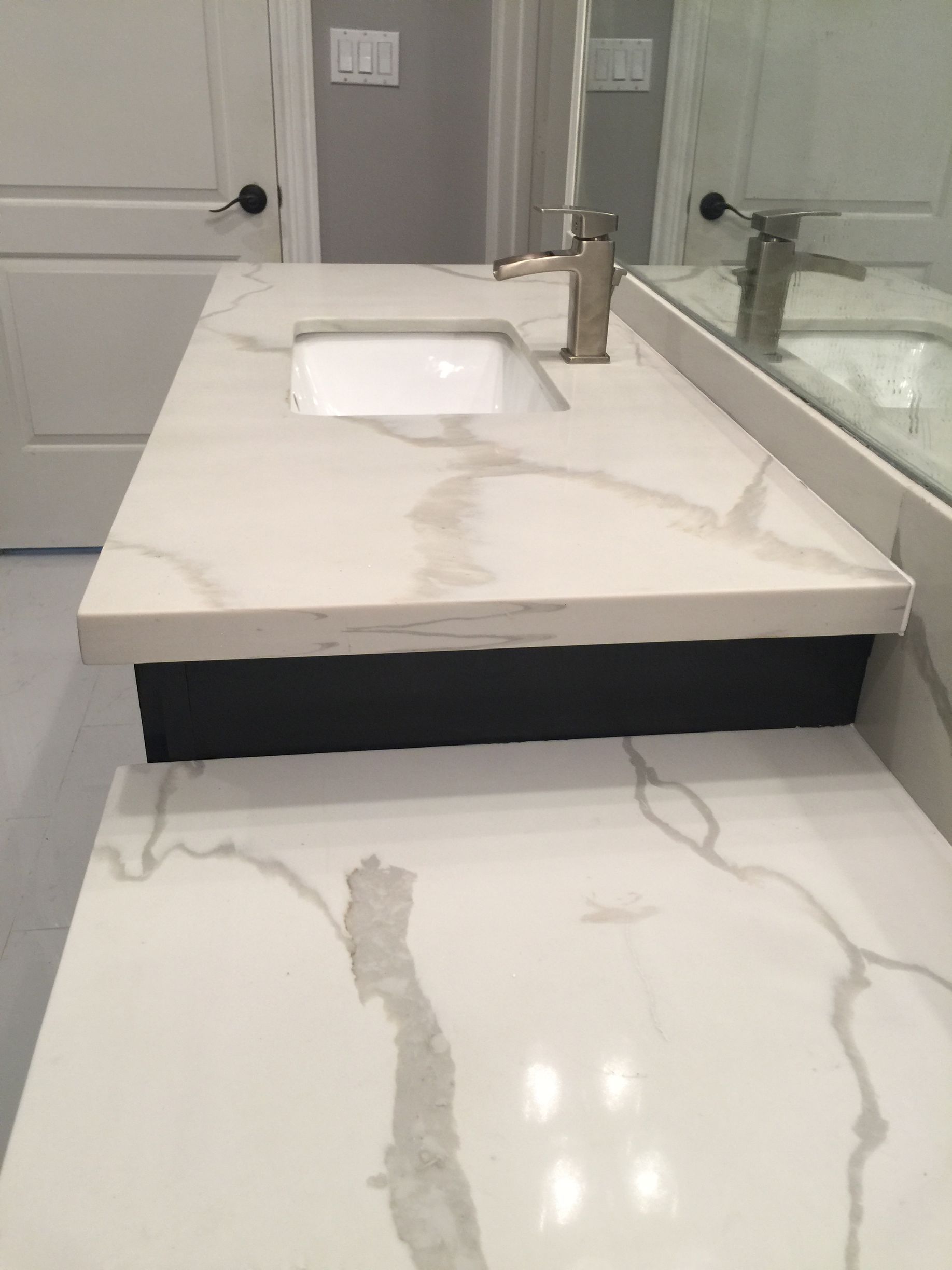 White marble countertop with a rectangular sink, black base, and a gold faucet.