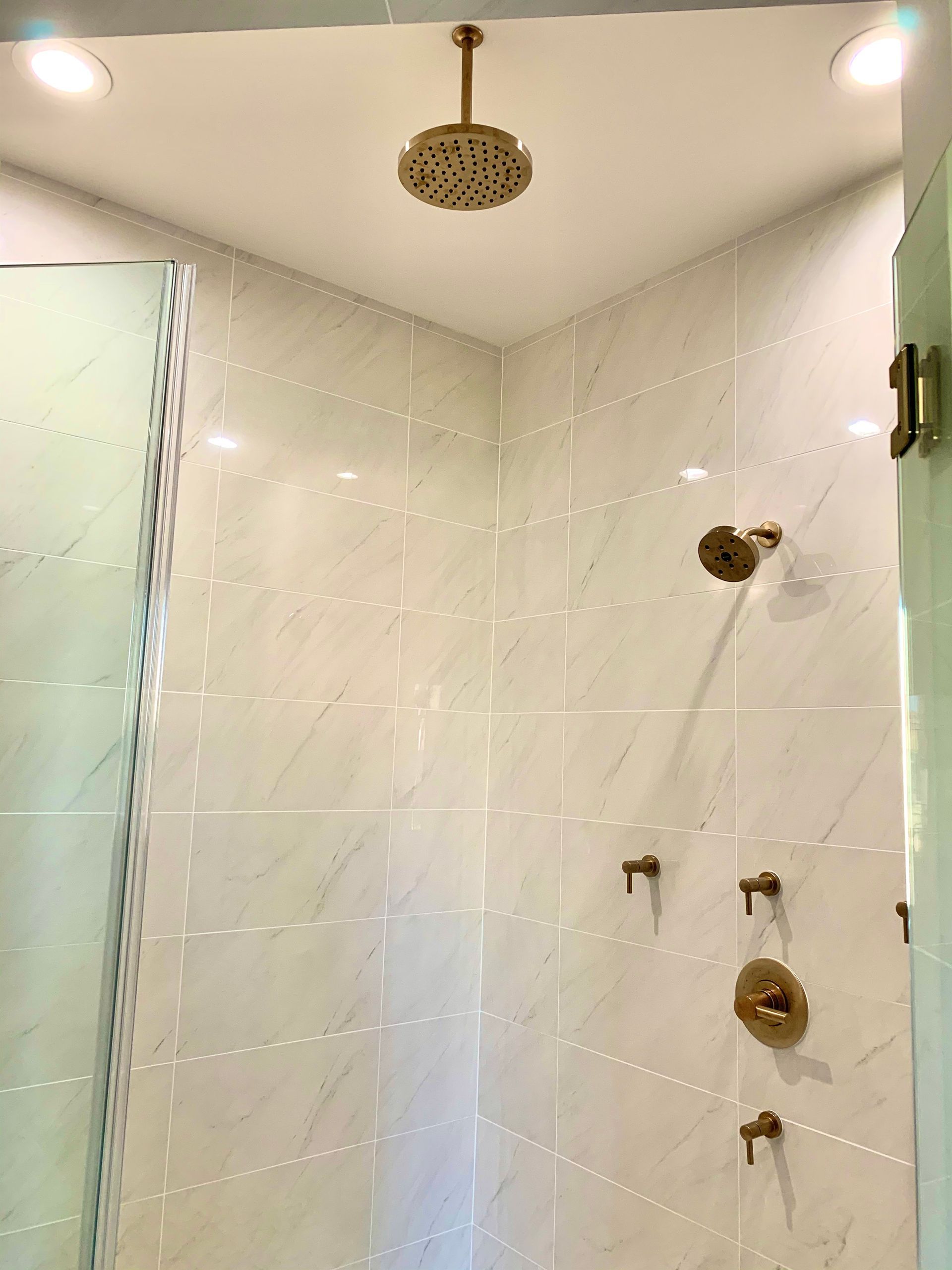 Gold shower fixtures in a white-tiled corner shower. 