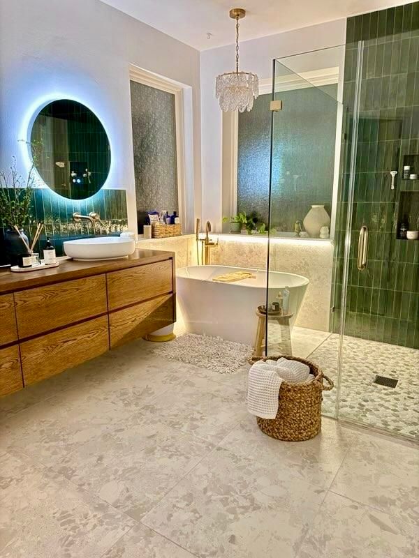 Luxurious bathroom with wood vanity, green shower tile, and a chandelier.