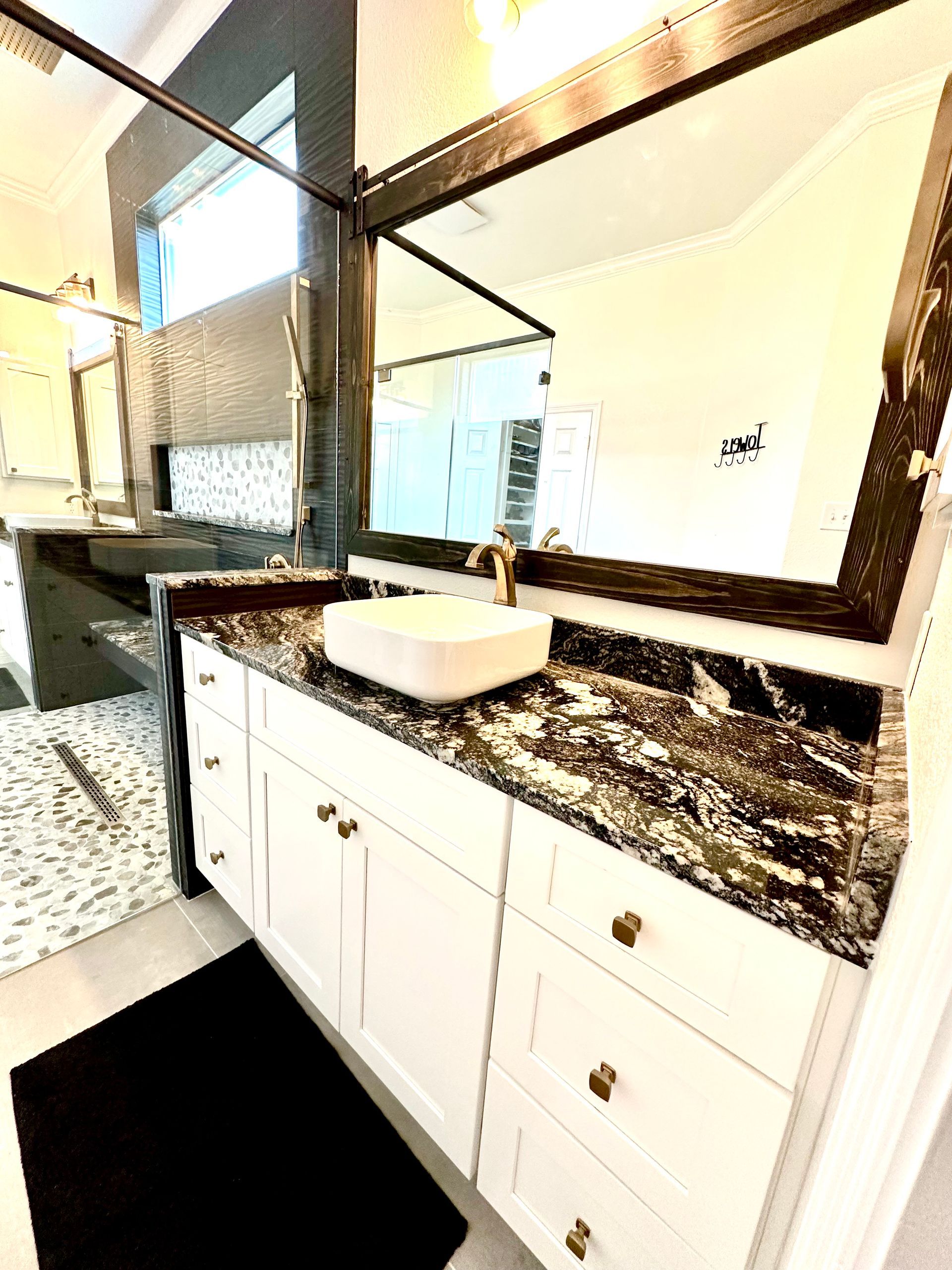 White bathroom vanity with black granite countertop, gold hardware, and large mirror.