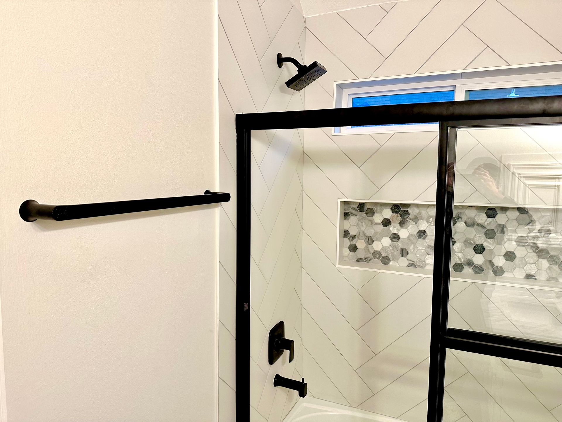 Modern bathroom with black framed shower, white tile, and mosaic accent.